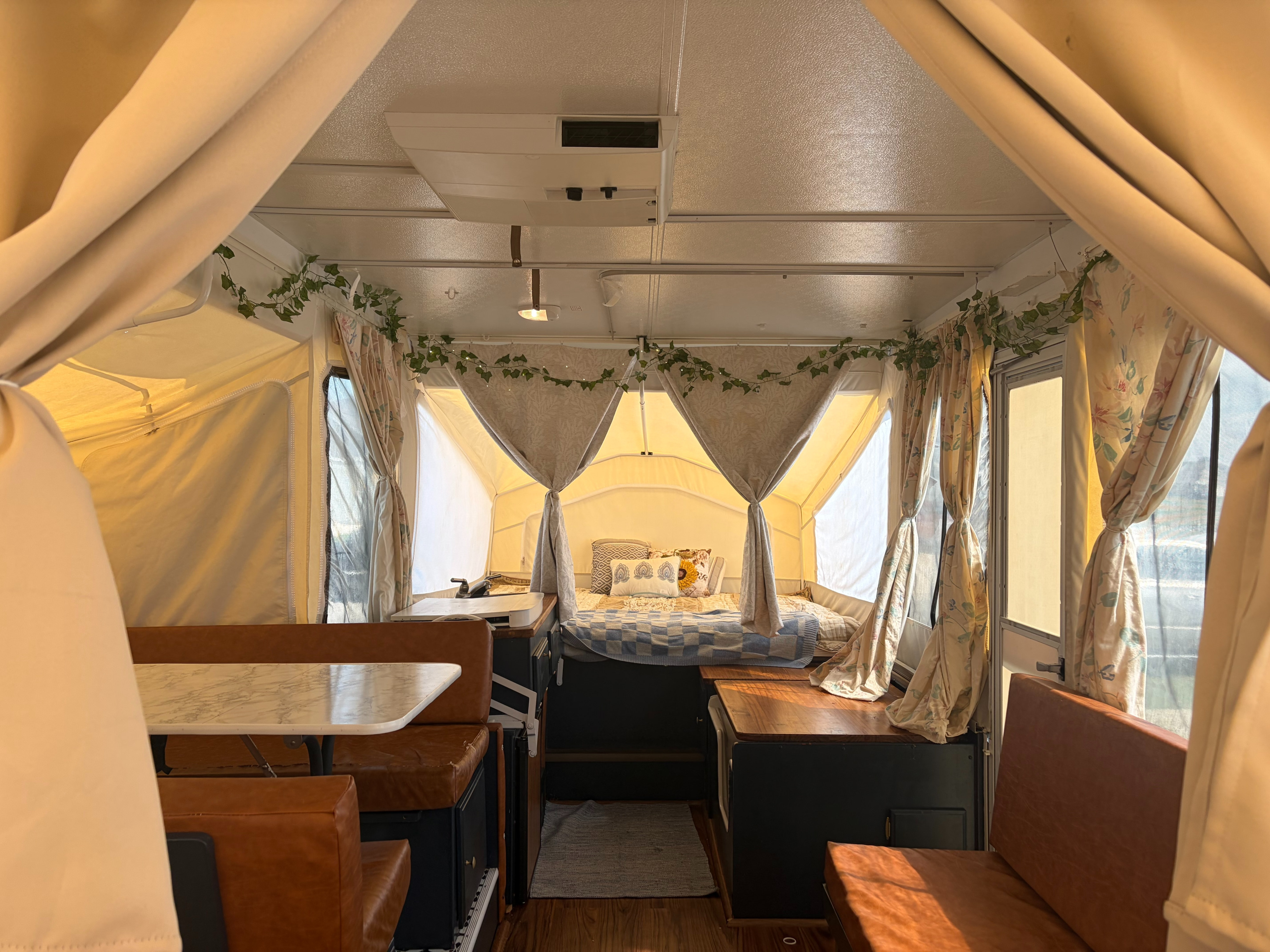 Cozy pop-up RV rental interior: bed, dining, and kitchenette, decorated with ivy & floral curtains for a homey feel.. Rockwood Freedom 231 2014