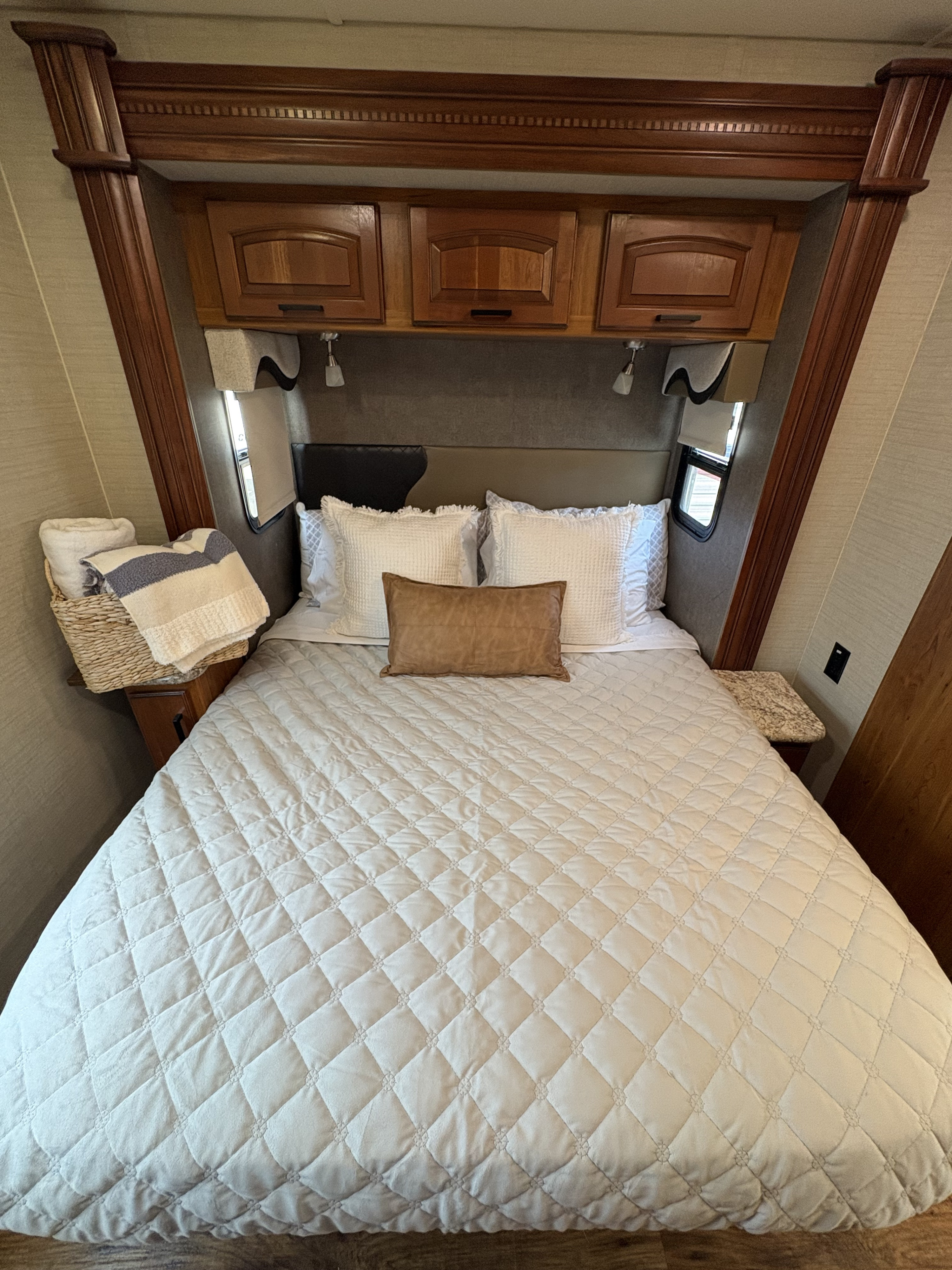 Cozy RV rental bedroom with quilted bedding, wood cabinets, side tables, and neatly folded towels in a basket.. Jayco Precept 2017