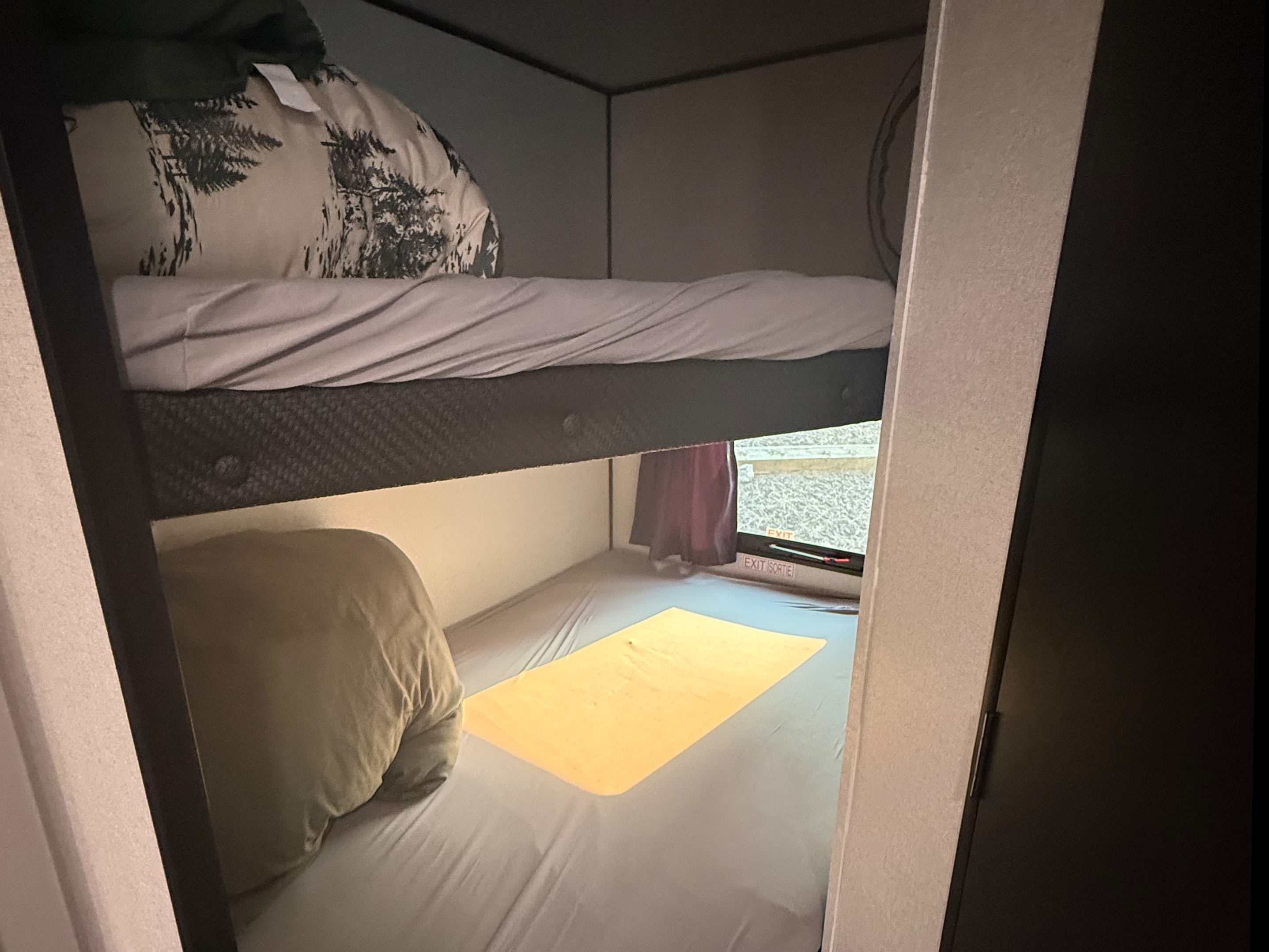 Bunk beds inside an RV rental, with a top bunk featuring a tree-patterned pillow and a bottom bunk with a yellow mat and exit window.. Jayco Jay Flight SLX 2026