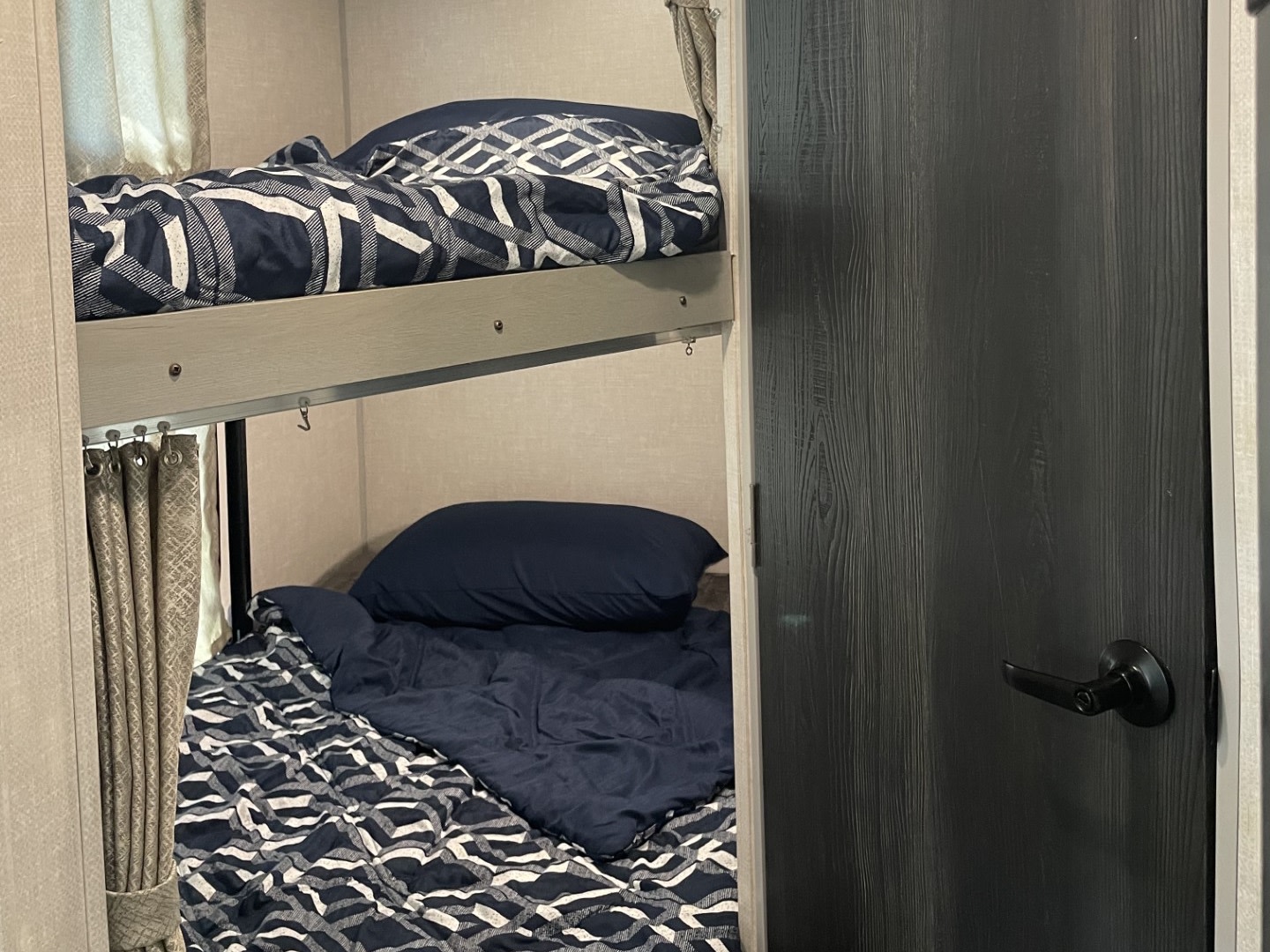 This RV rental features stacked bunk beds with navy blue bedding and patterned comforters, next to a dark wood-grain door.. Forest River Ibex 2022