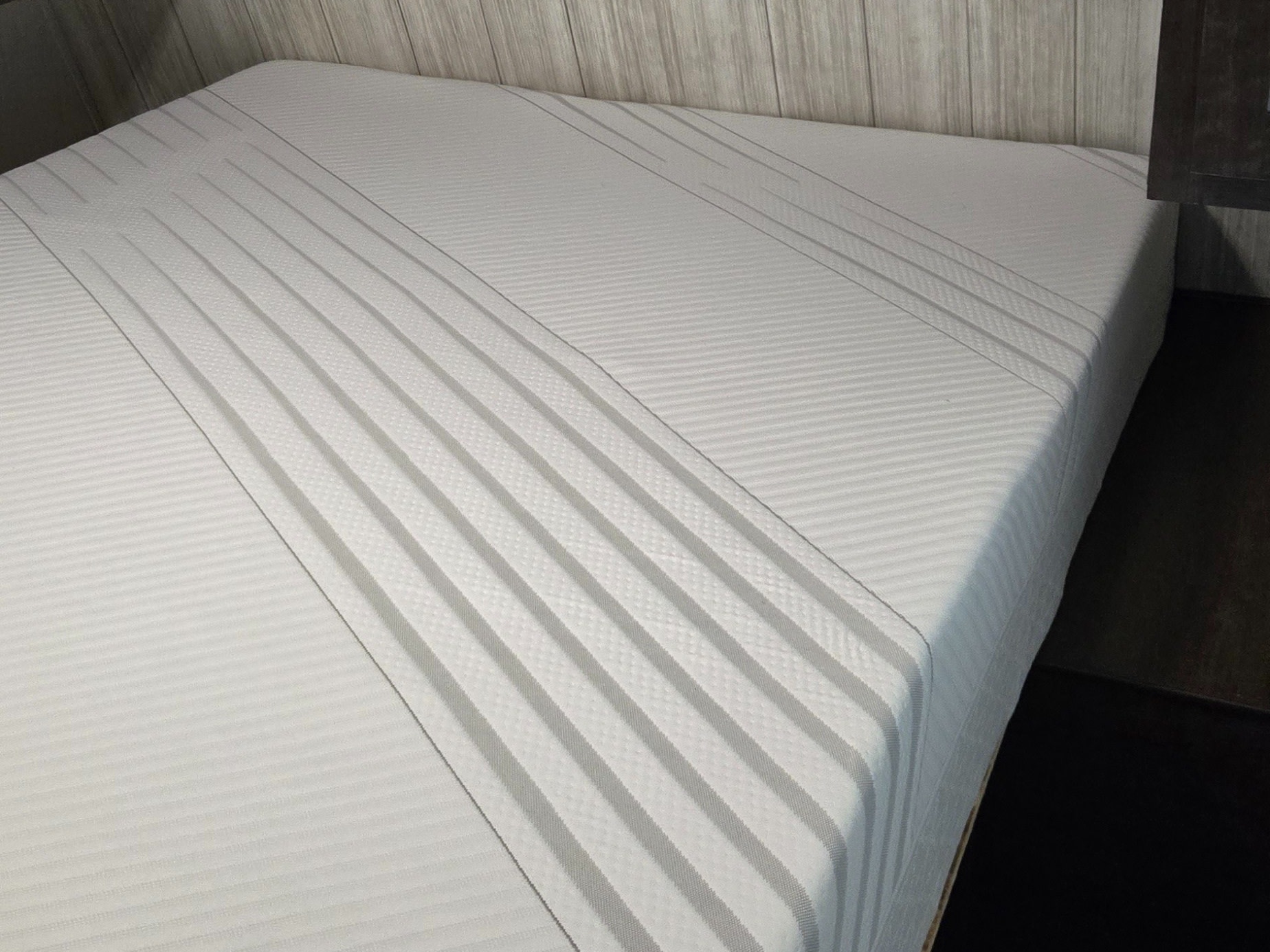 Inside an RV rental: a cozy bedroom features a striped white mattress, wood-paneled headboard, and overhead cabinets.. Heartland RVs Pioneer 2020