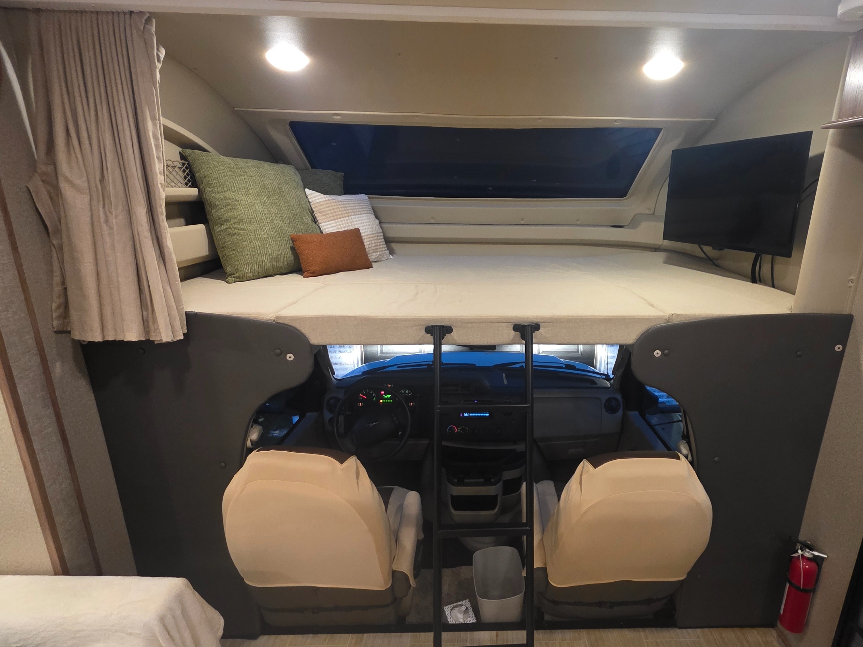 RV rental interior: cozy overhead bunk bed with TV, showing the driver's cab below and a ladder.. Entegra Coach Odyssey 2020