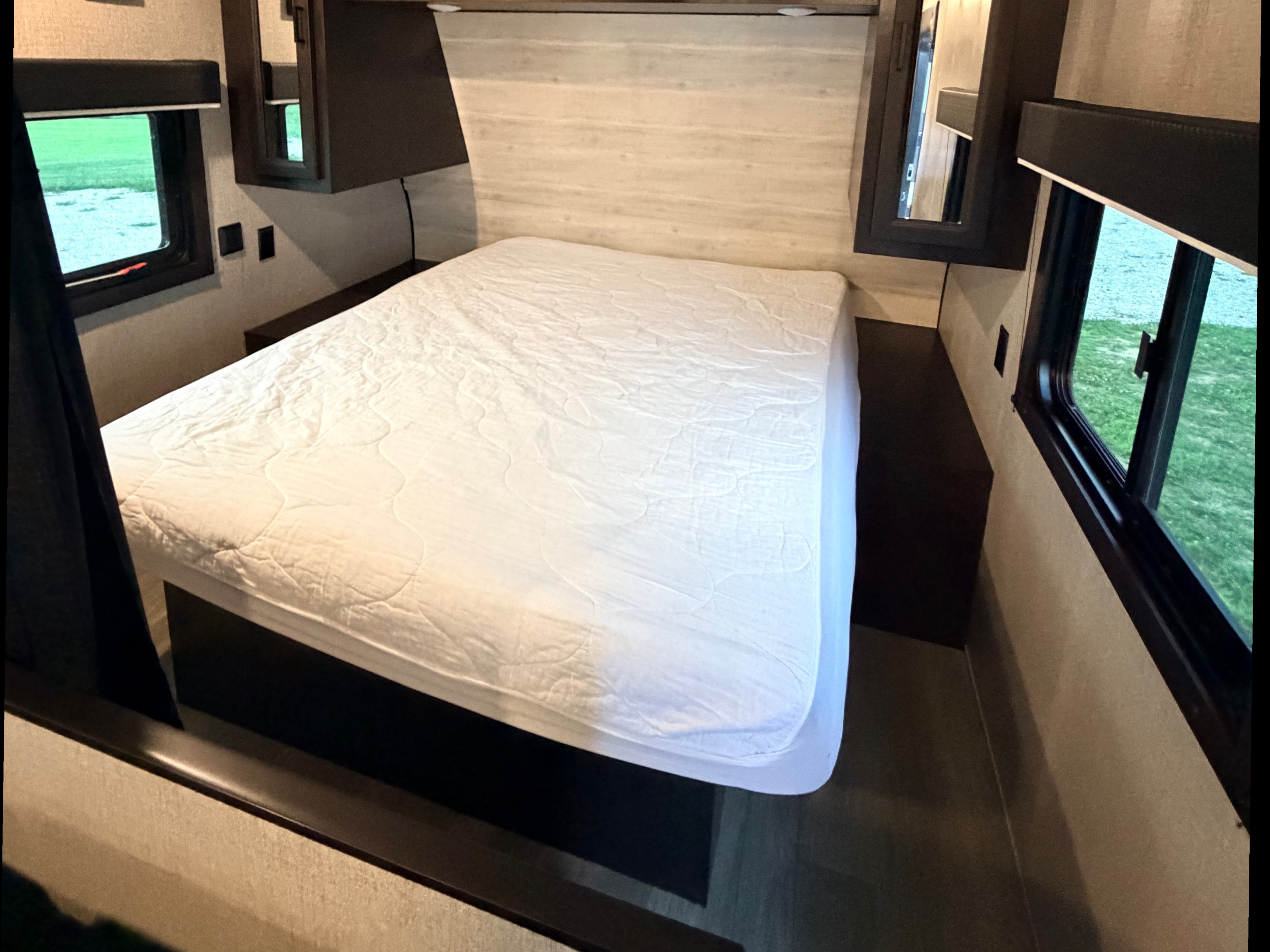 This RV rental bedroom features a white bed, overhead storage, and windows revealing outdoor scenery, offering a comfortable travel space.. Jayco Jay Flight SLX 2022