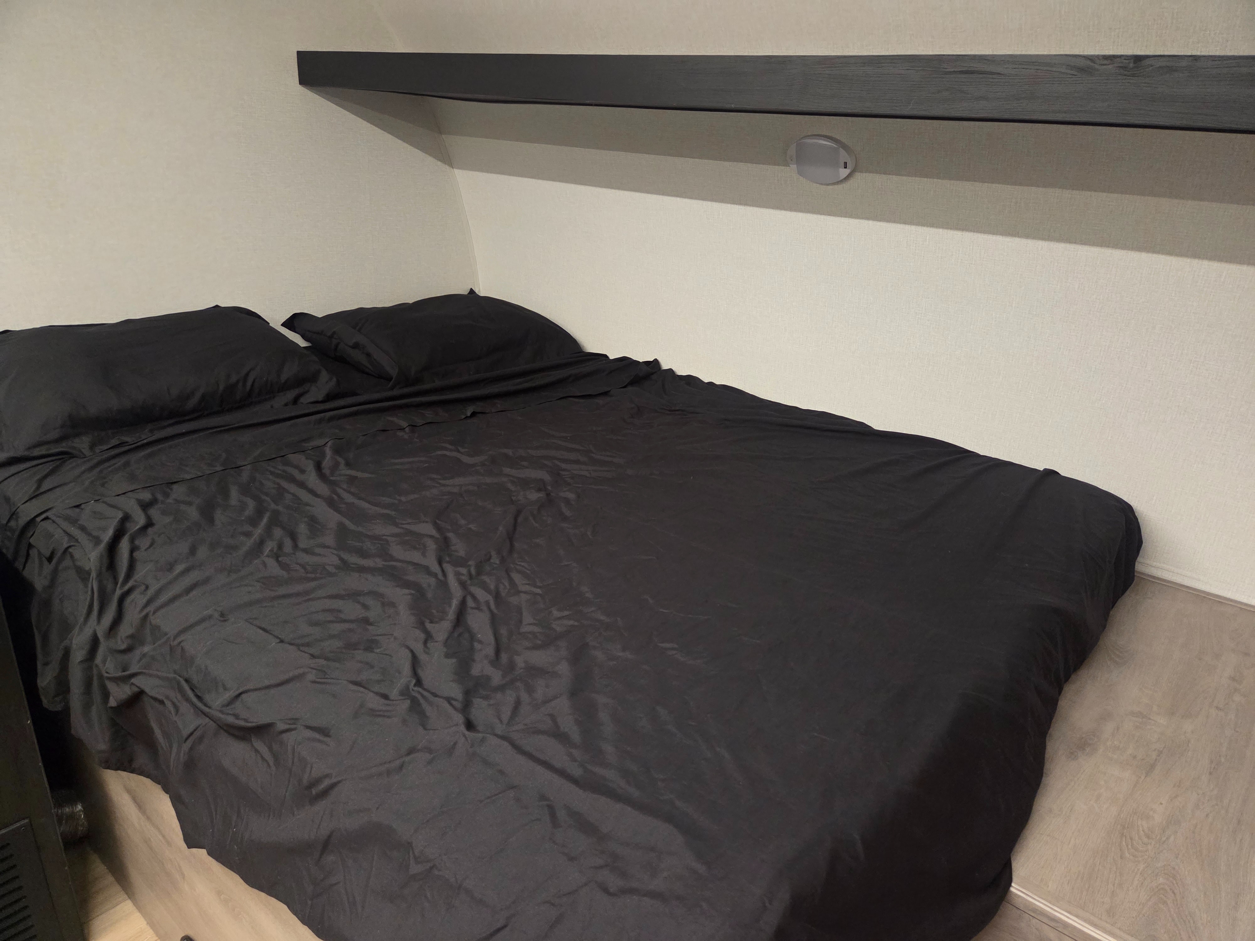 Cozy RV rental bedroom with black sheets, pillows, overhead shelf, and integrated light/USB ports.. Cruiser RV Embrace 2025