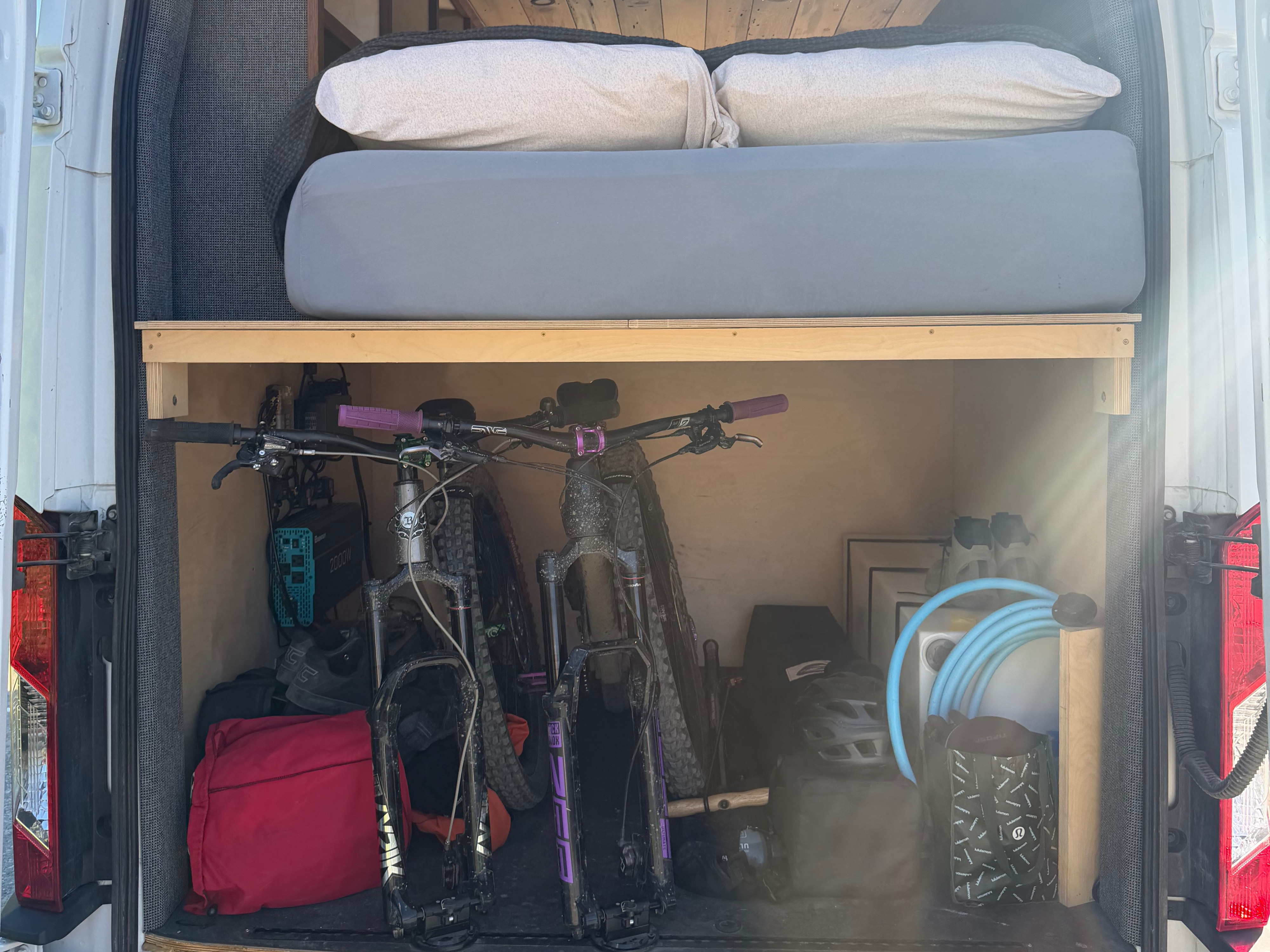 Ultimate RV rental setup: van's rear storage holds two mountain bikes and gear, with a comfortable bed overhead.. Ford Transit 2023