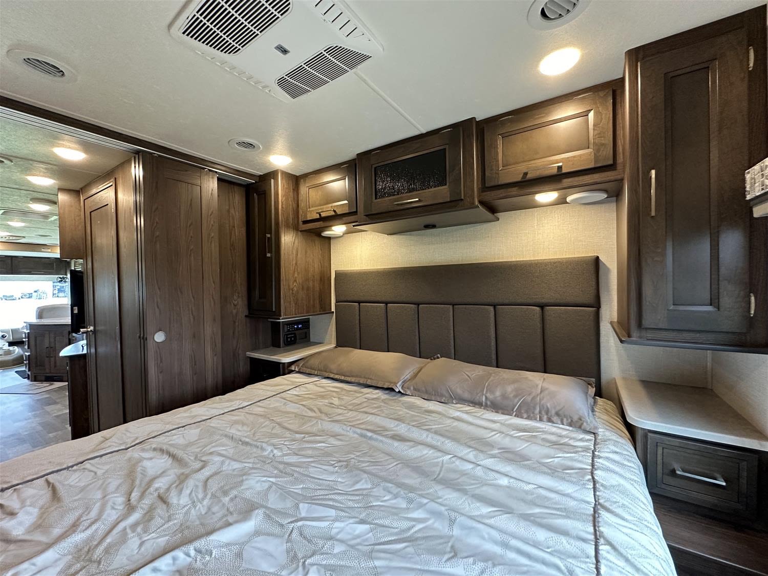 Relaxing rv rental bedroom: large bed, sleek dark wood cabinets, comfy padded headboard, and modern lighting.. Coachman Mirada 2018