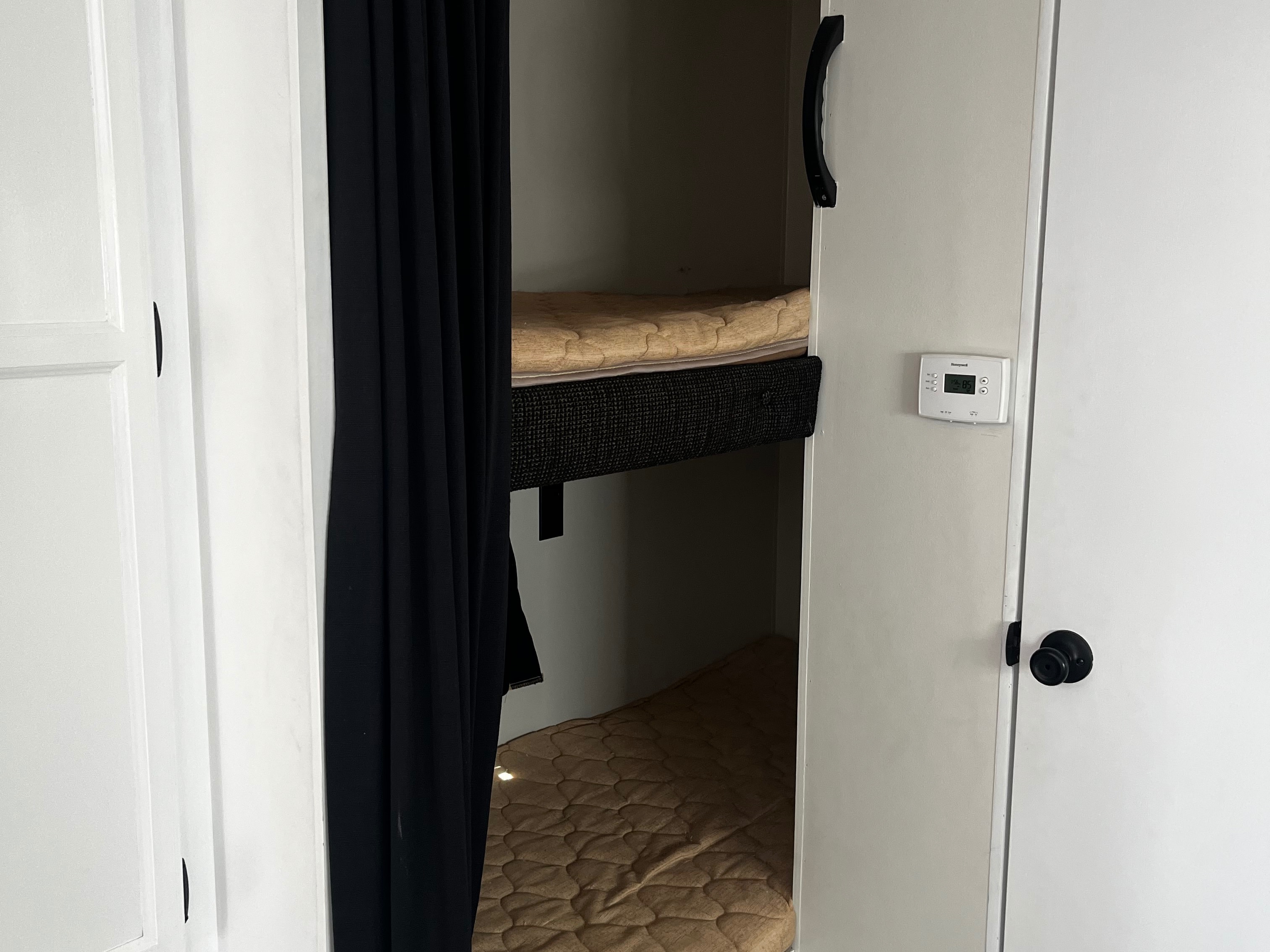 This rv rental features compact bunk beds with mattresses and black privacy curtains, along with a visible thermostat on the wall.. Starcraft AR-One Maxx 2015