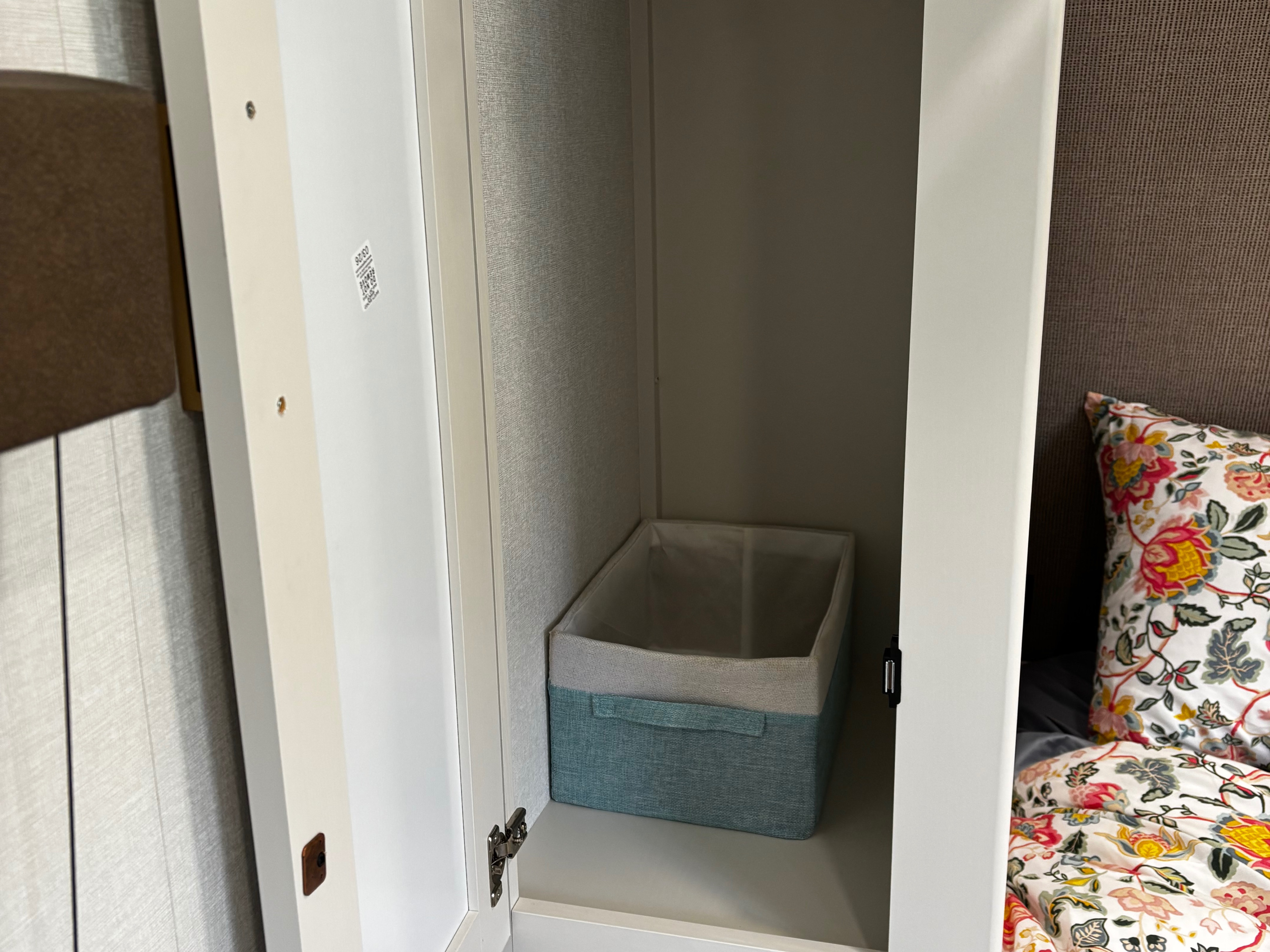 Compact storage in this RV rental bedroom: an open wardrobe with a storage basket next to a bed with floral bedding.. Grand Design Transcend Xplore 19bhx 2027