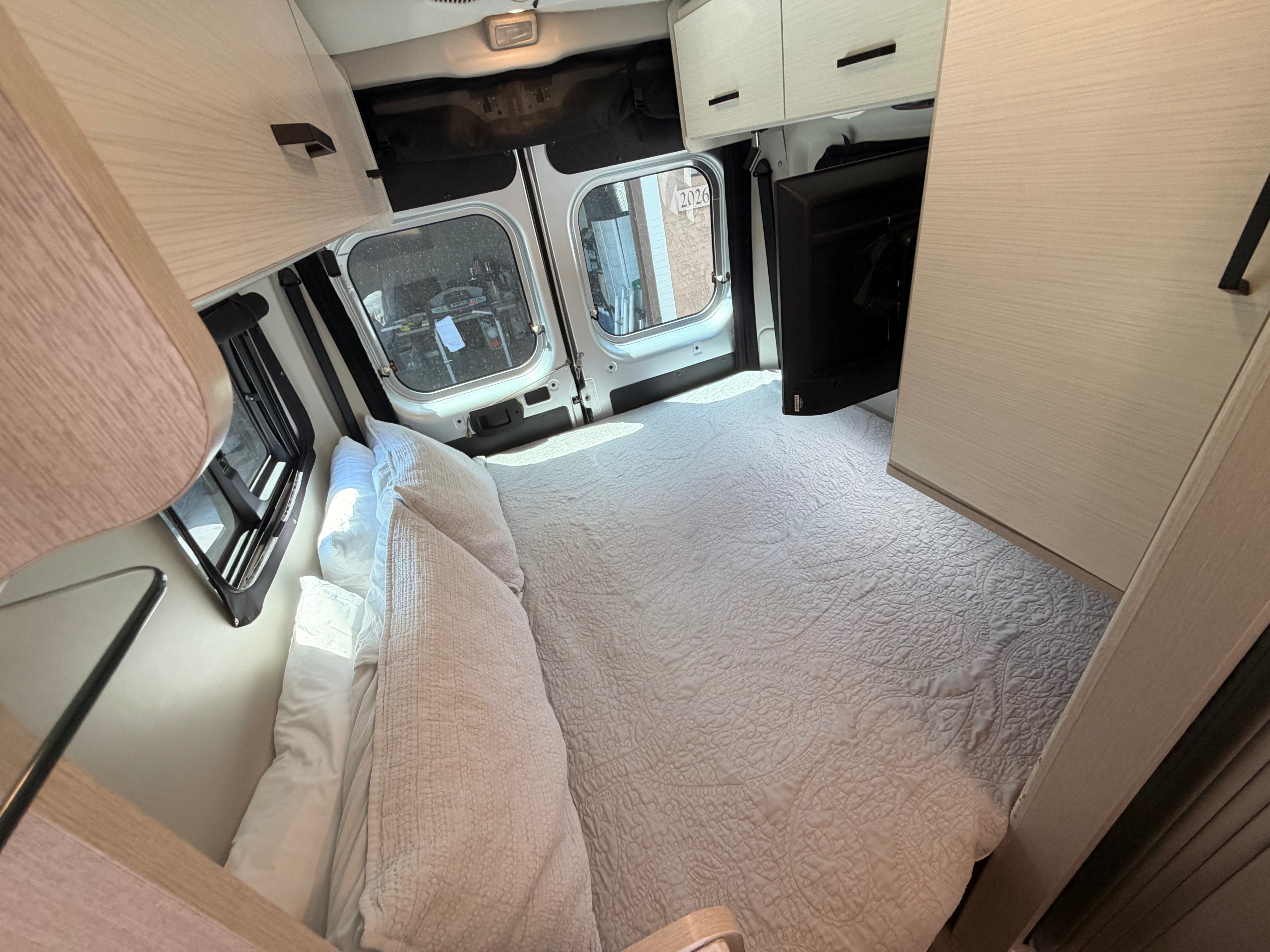 Interior of a clean rv rental camper van, featuring a cozy bed with light bedding, sleek wooden cabinets, and a mounted TV.. Dodge Ram 1500 2023