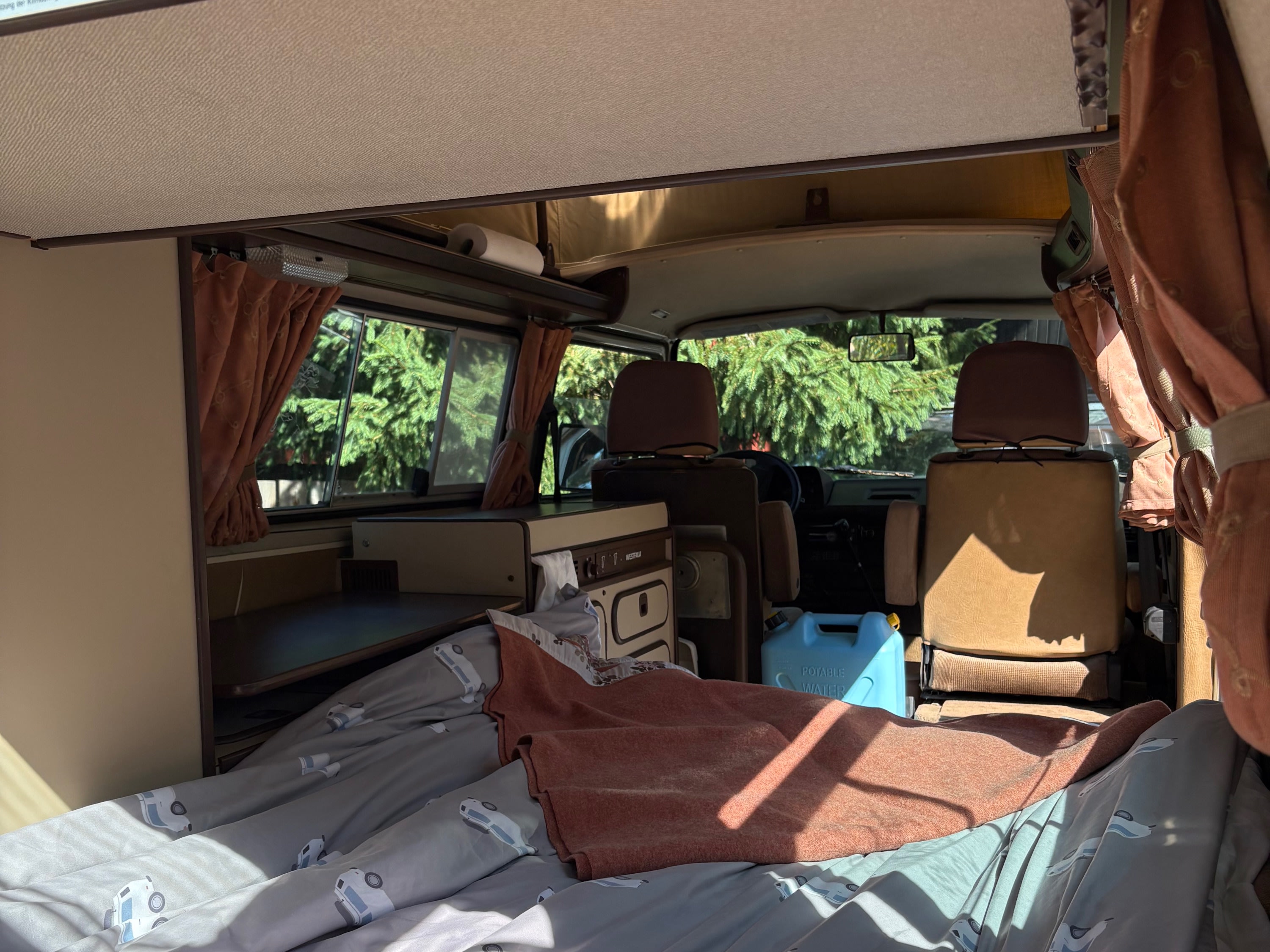 Cozy RV rental interior showing a comfortable bed, compact kitchen unit, and front cab area. Ready for road trips!. Westfalia T3 Westfalia 1986