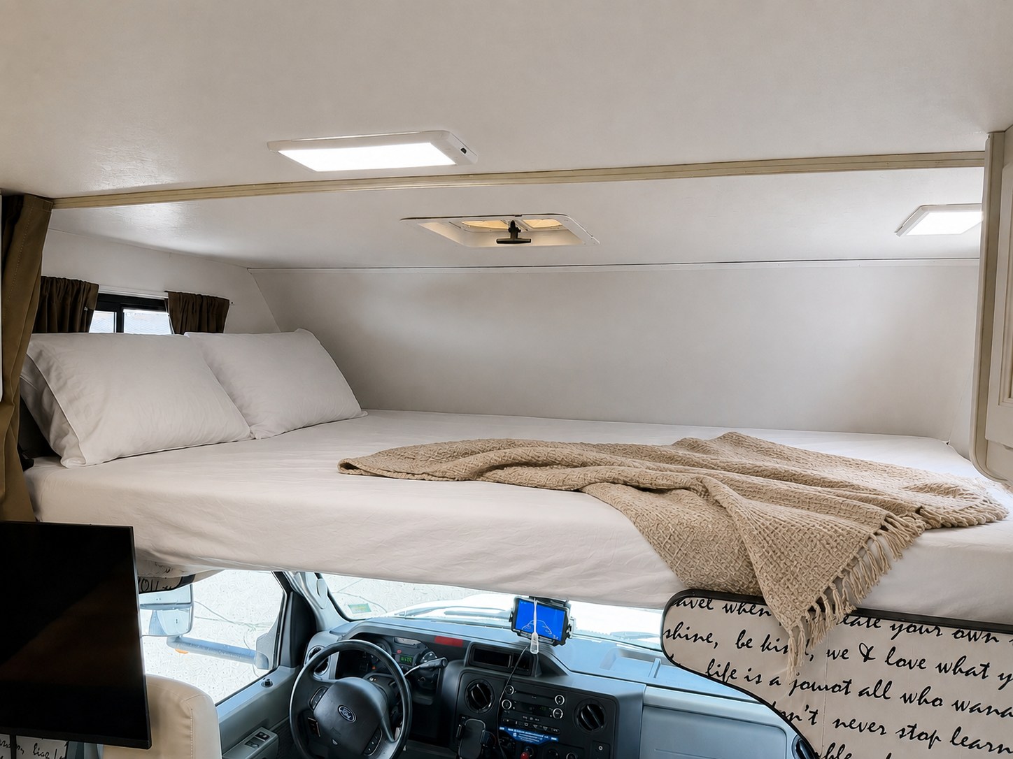 An RV rental's cozy cab-over sleeping area with a bed, pillows, and blanket, above the driver's cabin.. Thor Majestic 2015