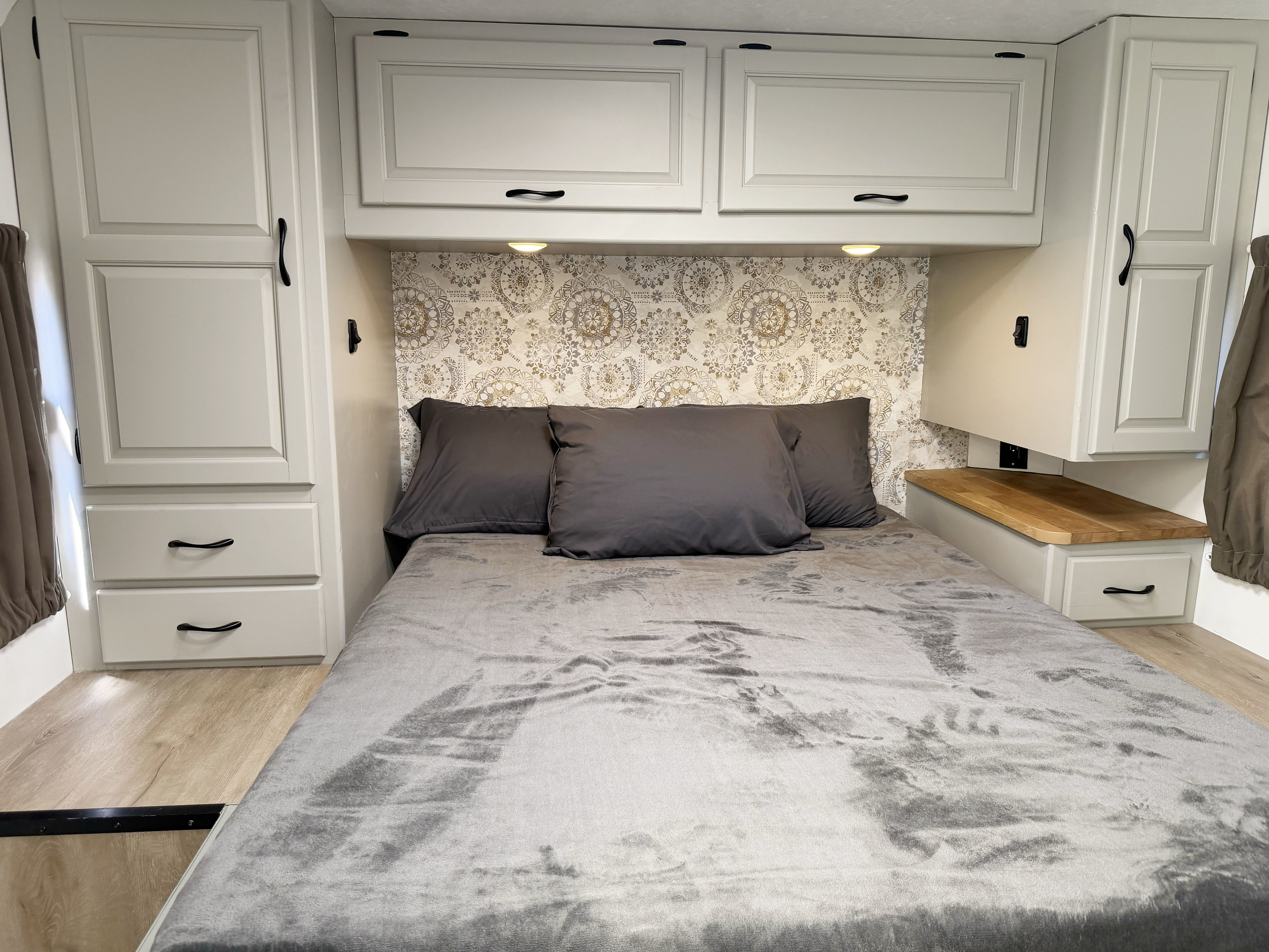 RV rental bedroom featuring a plush gray bed, ornate headboard wallpaper, light storage cabinets, and a wooden nightstand.. Thor Majestic 2015