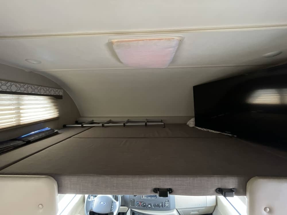 Overhead bunk bed in this cozy RV rental, with a comfy mattress, TV, and window. Ideal sleeping space for your motorhome journey.. Thor Freedom Elite 2020