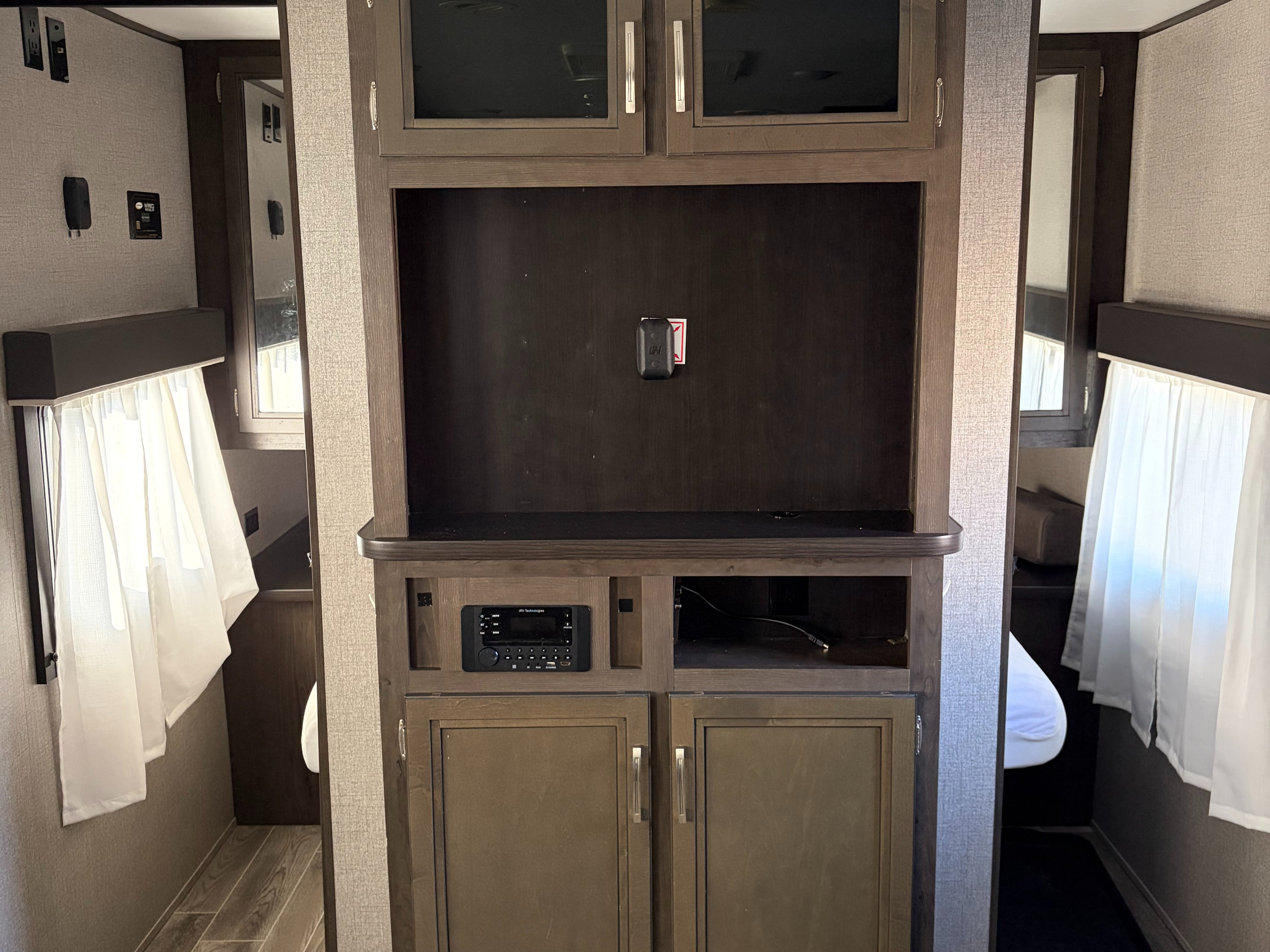 RV rental: Interior view of an entertainment center with empty TV mount, iRV stereo, and storage cabinets, flanked by curtained doorways.. Jayco Jay Flight SLX Rocky Mountain Edition 2021