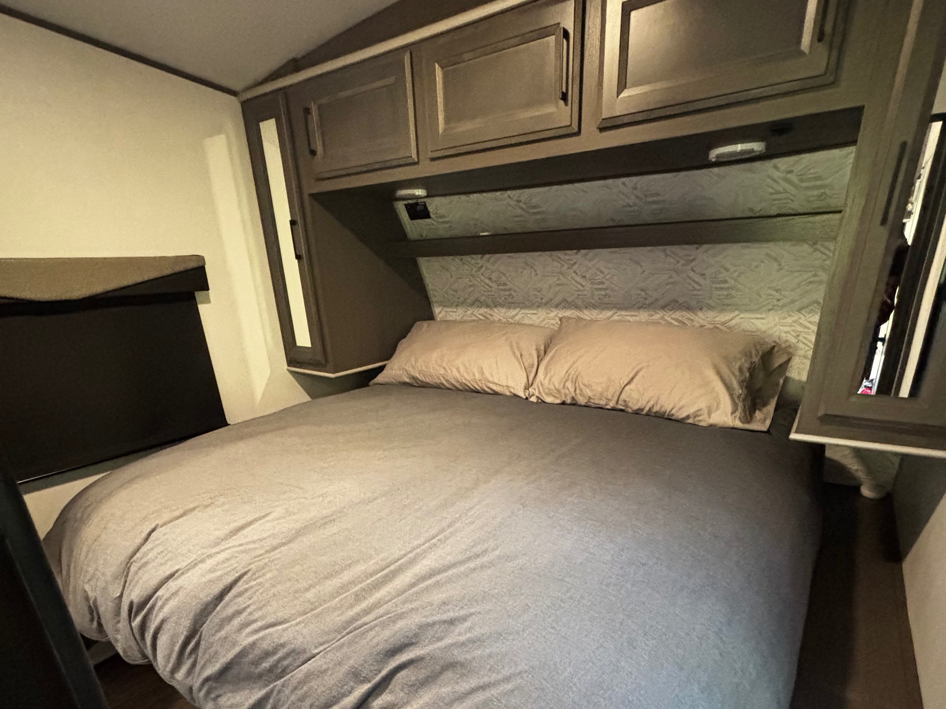 Cozy RV rental bedroom with a large bed, beige pillows, patterned headboard, and overhead storage cabinets.. Cruiser Rv Corp Stryker 2021