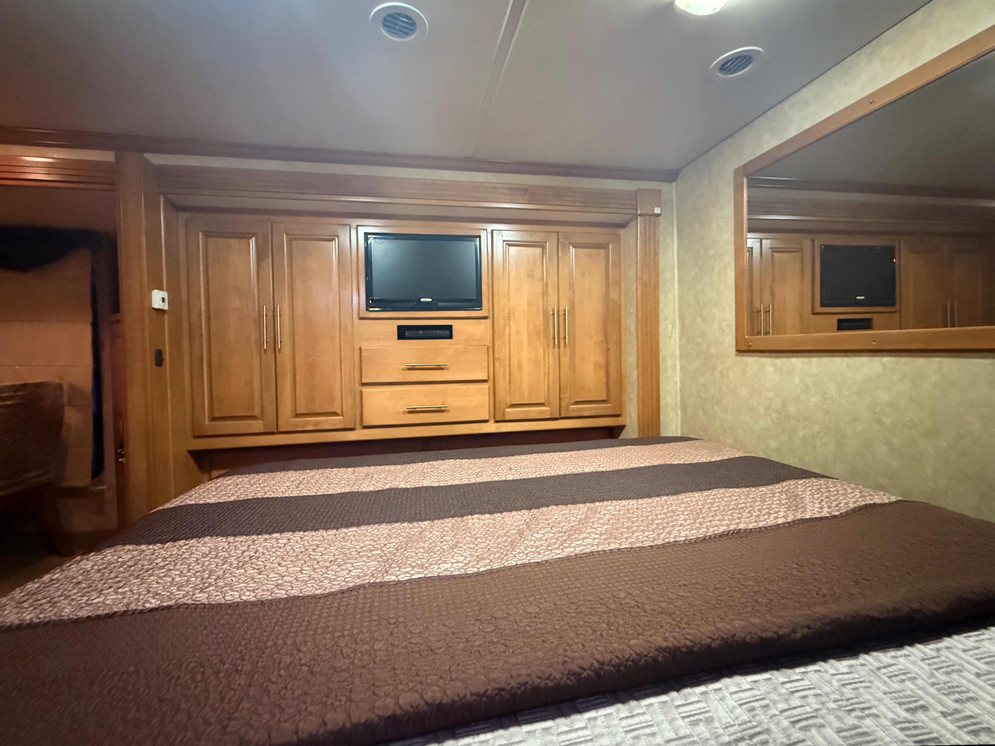 RV rental bedroom with a striped bedspread, built-in wooden cabinets, TV, and mirror for a comfortable stay.. Ford Coachmen Encounter 2012