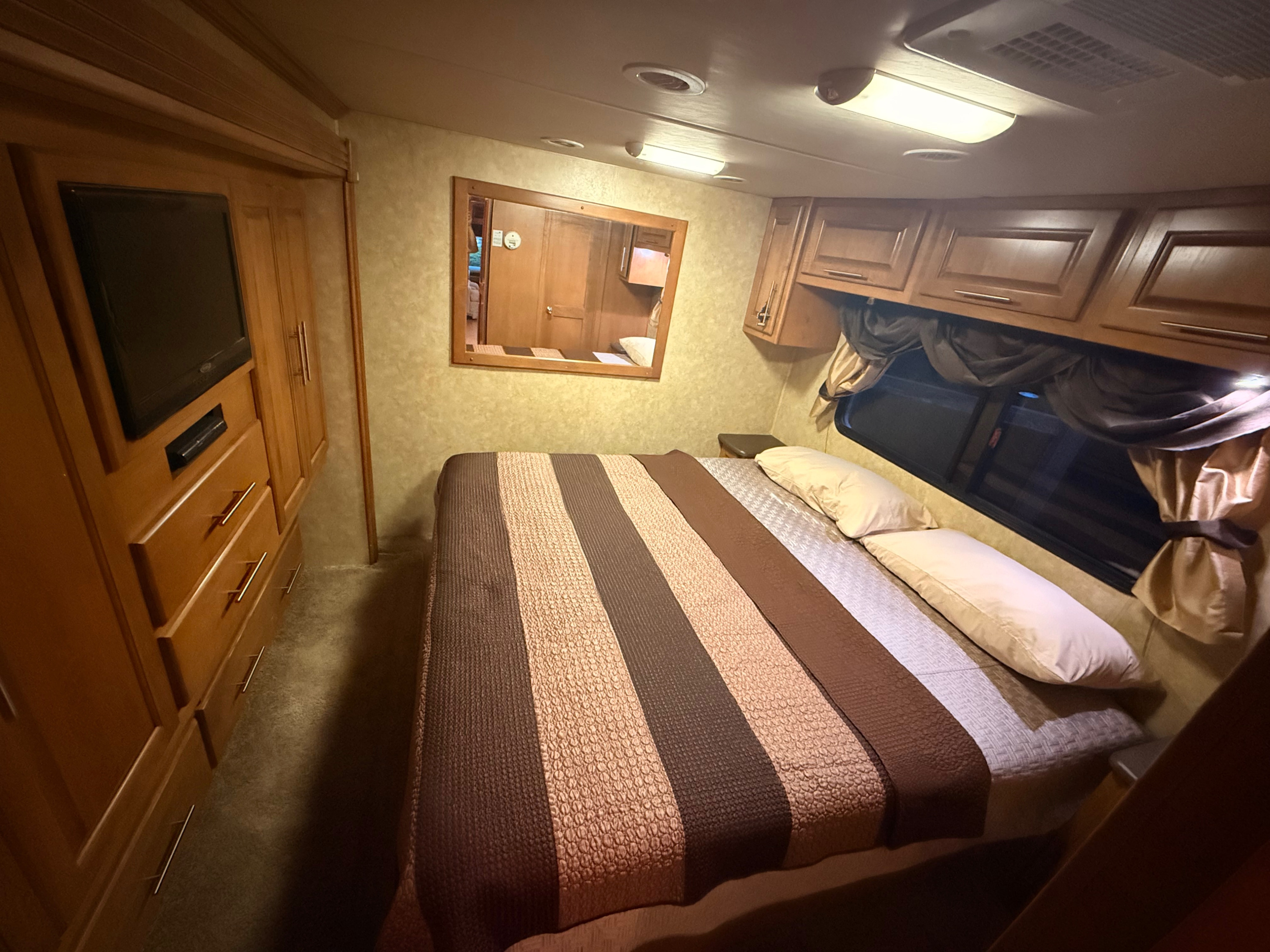 RV rental bedroom with a comfy striped bed, wood cabinetry, TV, and mirror for a homey feel.. Ford Coachmen Encounter 2012