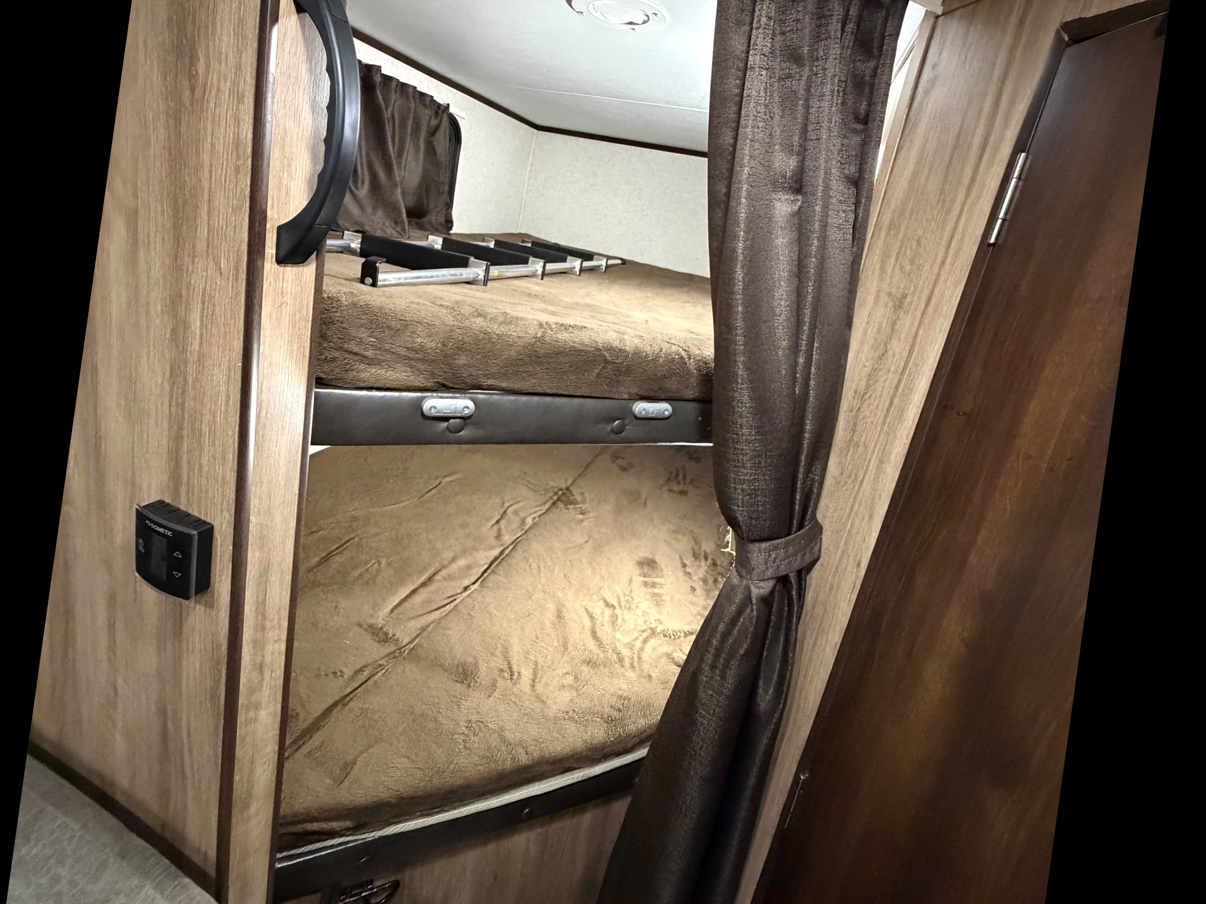 RV rental interior showing bunk beds with a ladder, warm brown bedding, a Dometic control panel, and wood paneling.. Jayco Jay Feather 2019