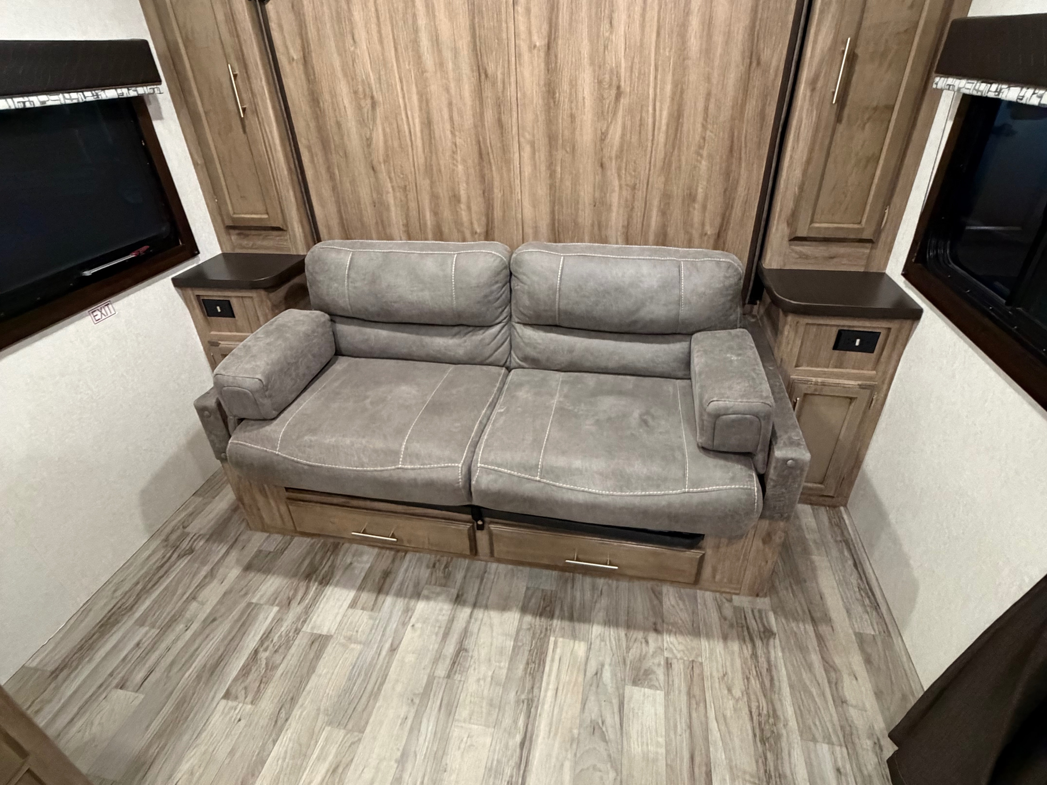Comfortable gray sleeper sofa with storage in an RV rental living area, flanked by wood cabinets & laminate flooring.. Jayco Jay Feather 2019