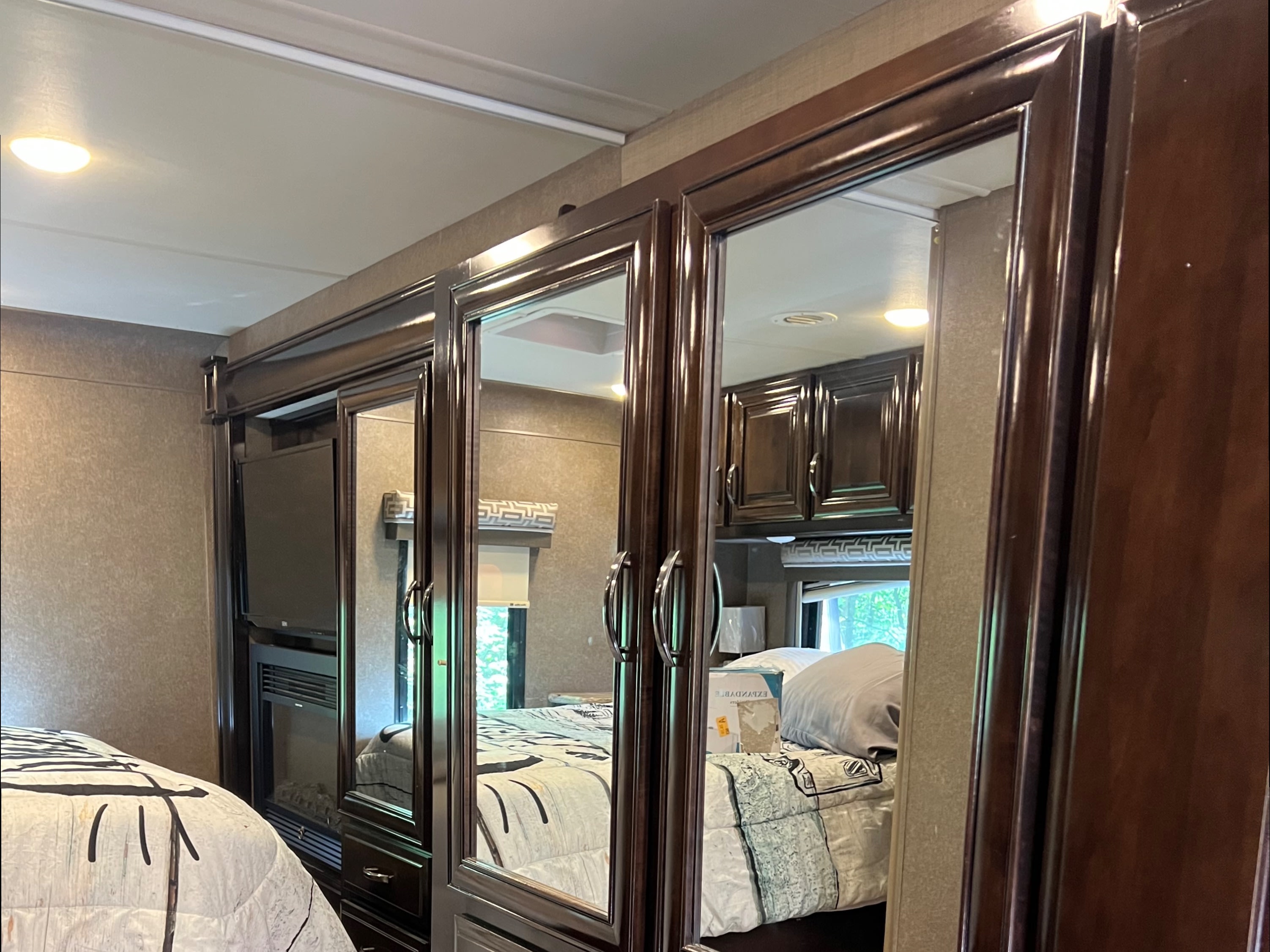 Discover comfort in this RV rental bedroom featuring dark wood mirrored cabinets, a built-in TV, and a cozy bed with laminate flooring.. Thor Quantum 2017
