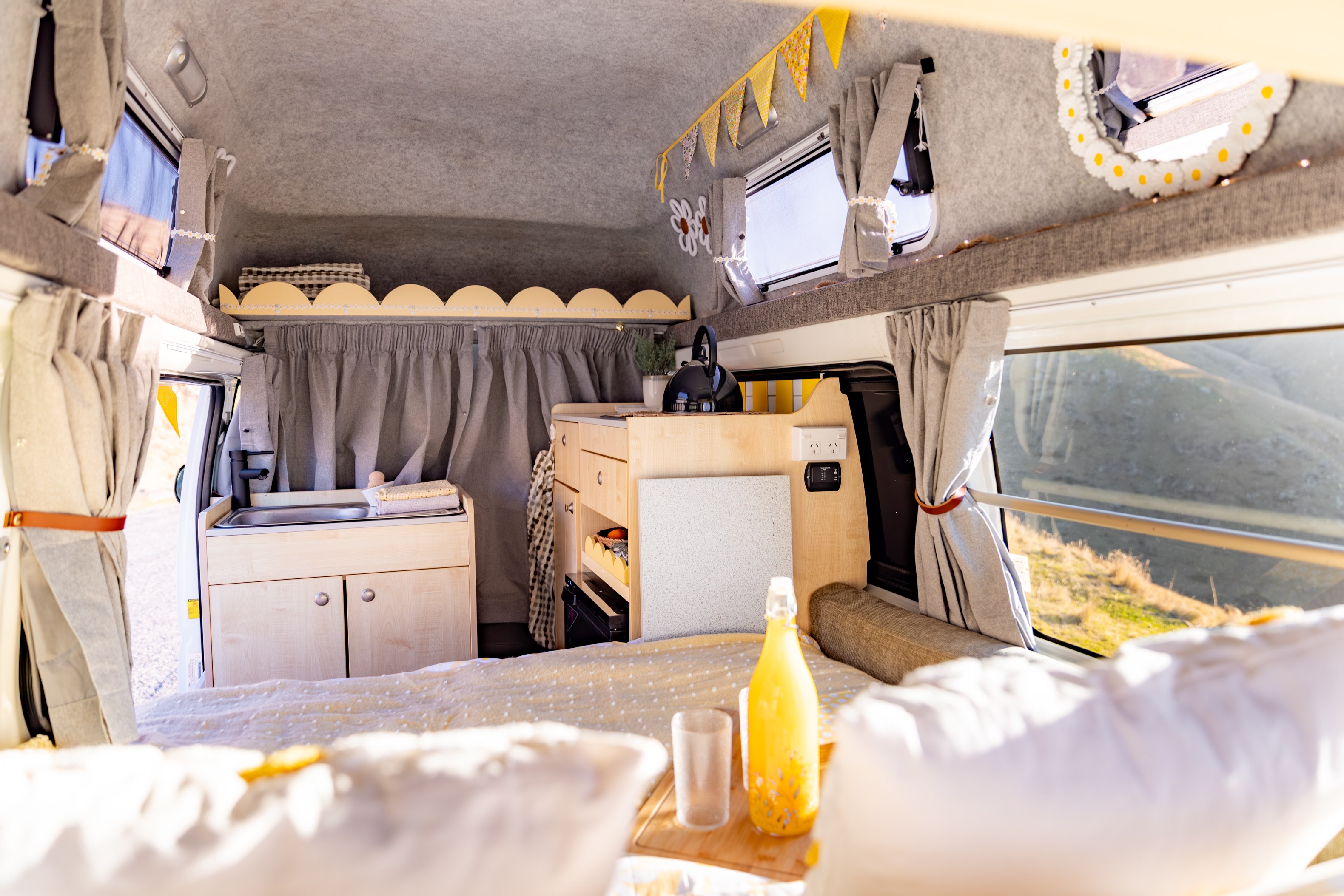 Bright and cozy rv rental interior featuring a small kitchen, bed, windows, and decorative elements for a comfortable journey.. Toyota Hiace 2013