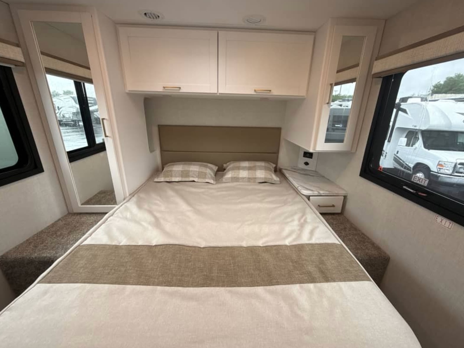 Cozy RV rental bedroom with a full-size bed, overhead cabinets, and windows offering views outside. Perfect for mobile adventures.. Thor Eddie Bauer 2026