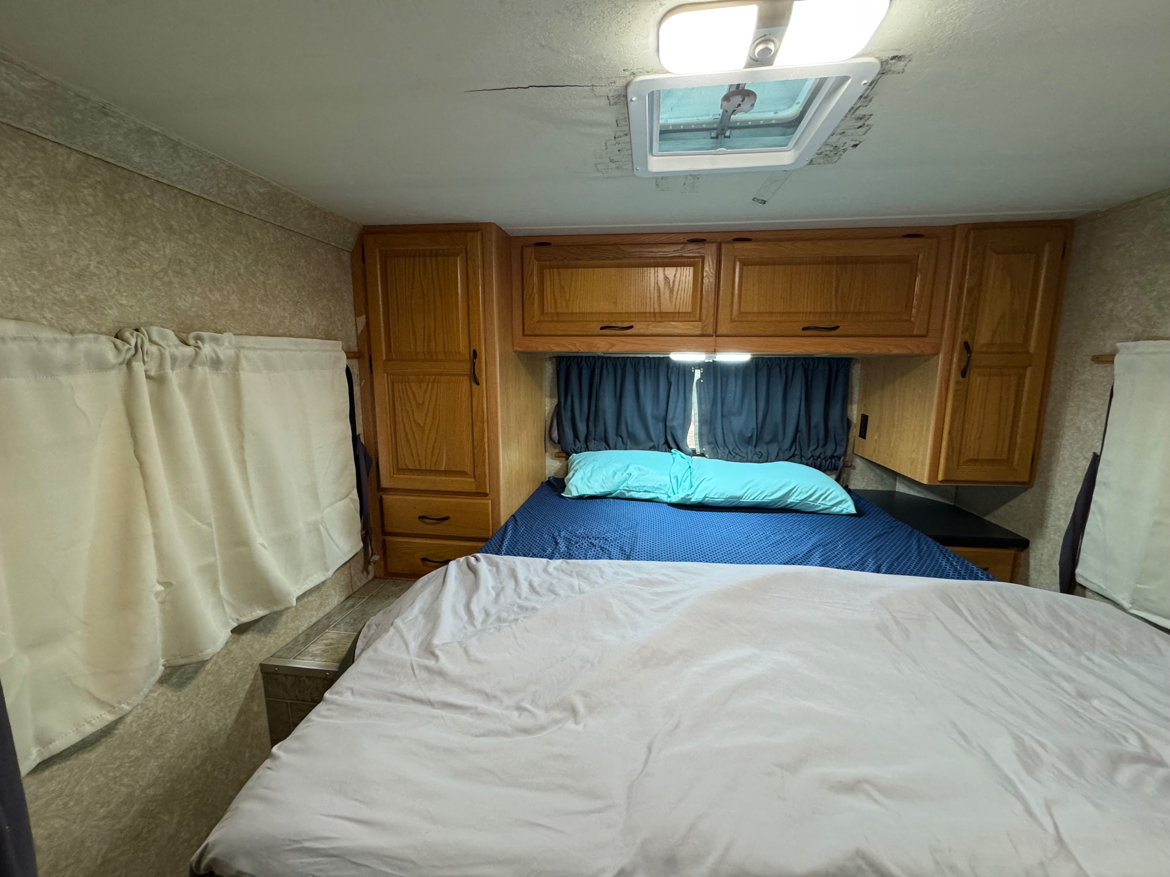RV rental bedroom interior: bed, wood cabinets, ceiling vent, & light fixture. Note the ceiling crack and water stains.. Four Winds Majestic 2008