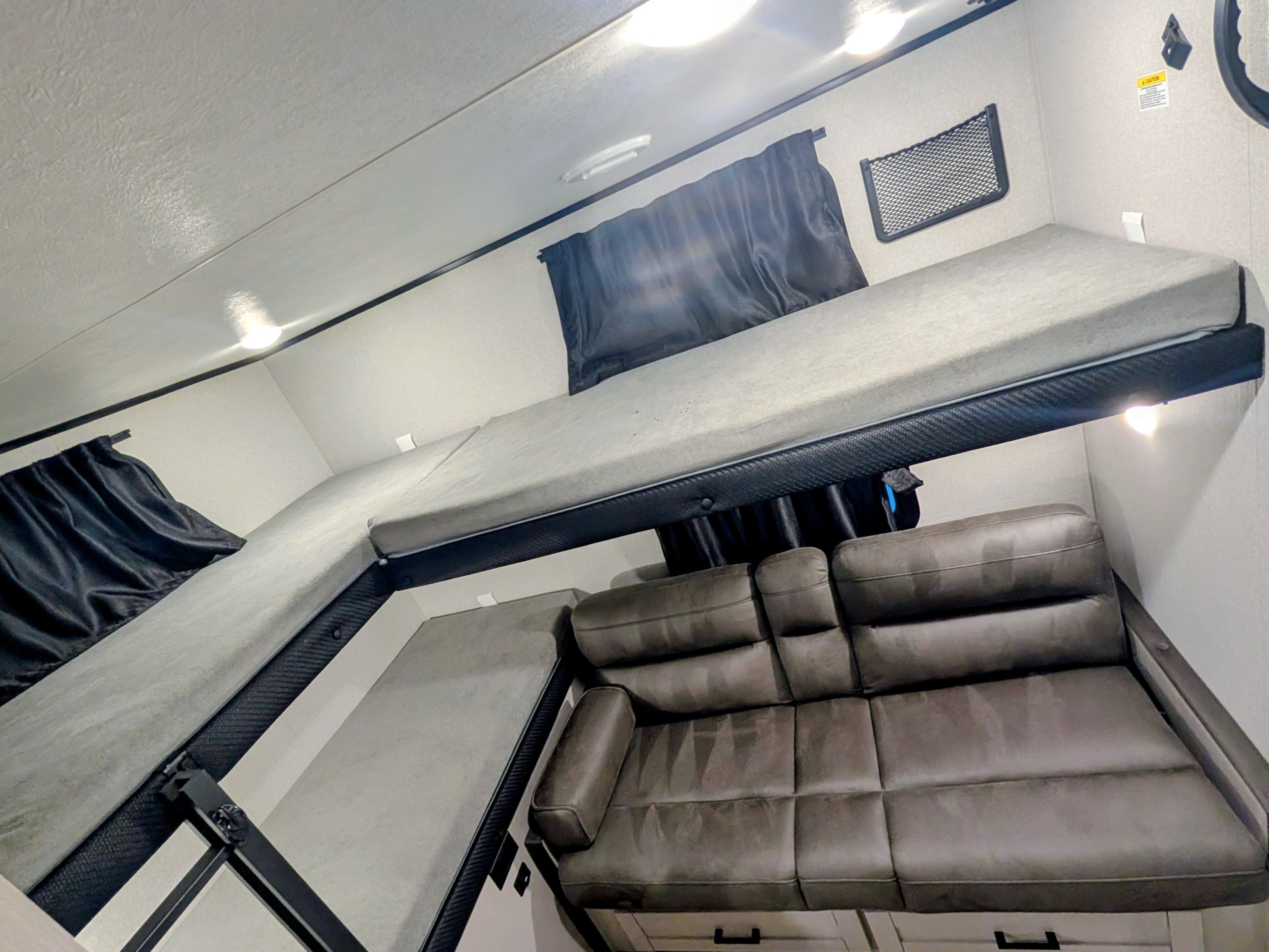 Bright RV rental interior features a convertible gray bunk bed system over a comfy brown leatherette sofa.. Jayco Jay Feather 2026