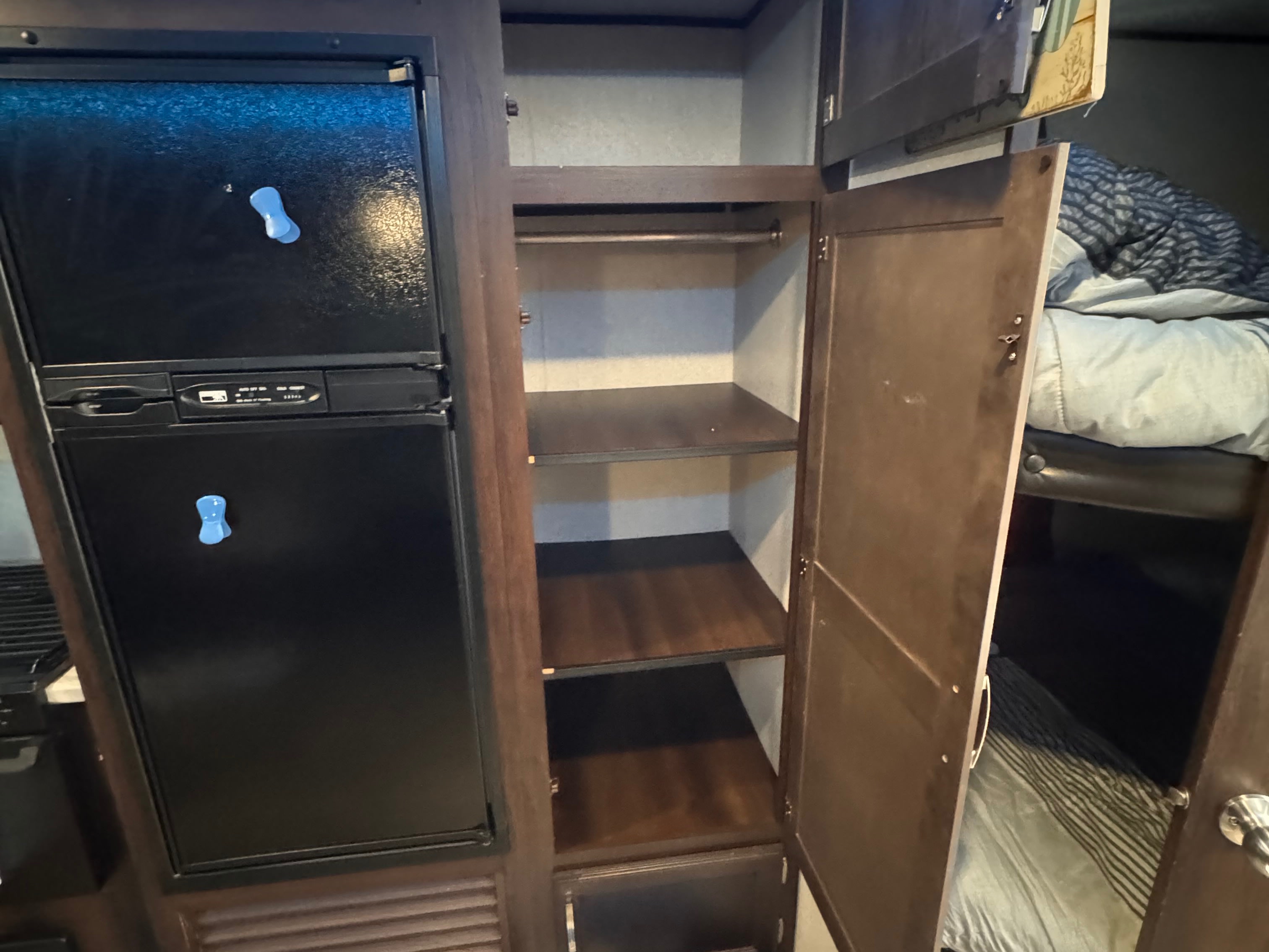Inside an RV rental: a black refrigerator, an open wardrobe with shelves, and a glimpse of a bunk bed with striped bedding.. Jayco Jay Flight SLX 2020