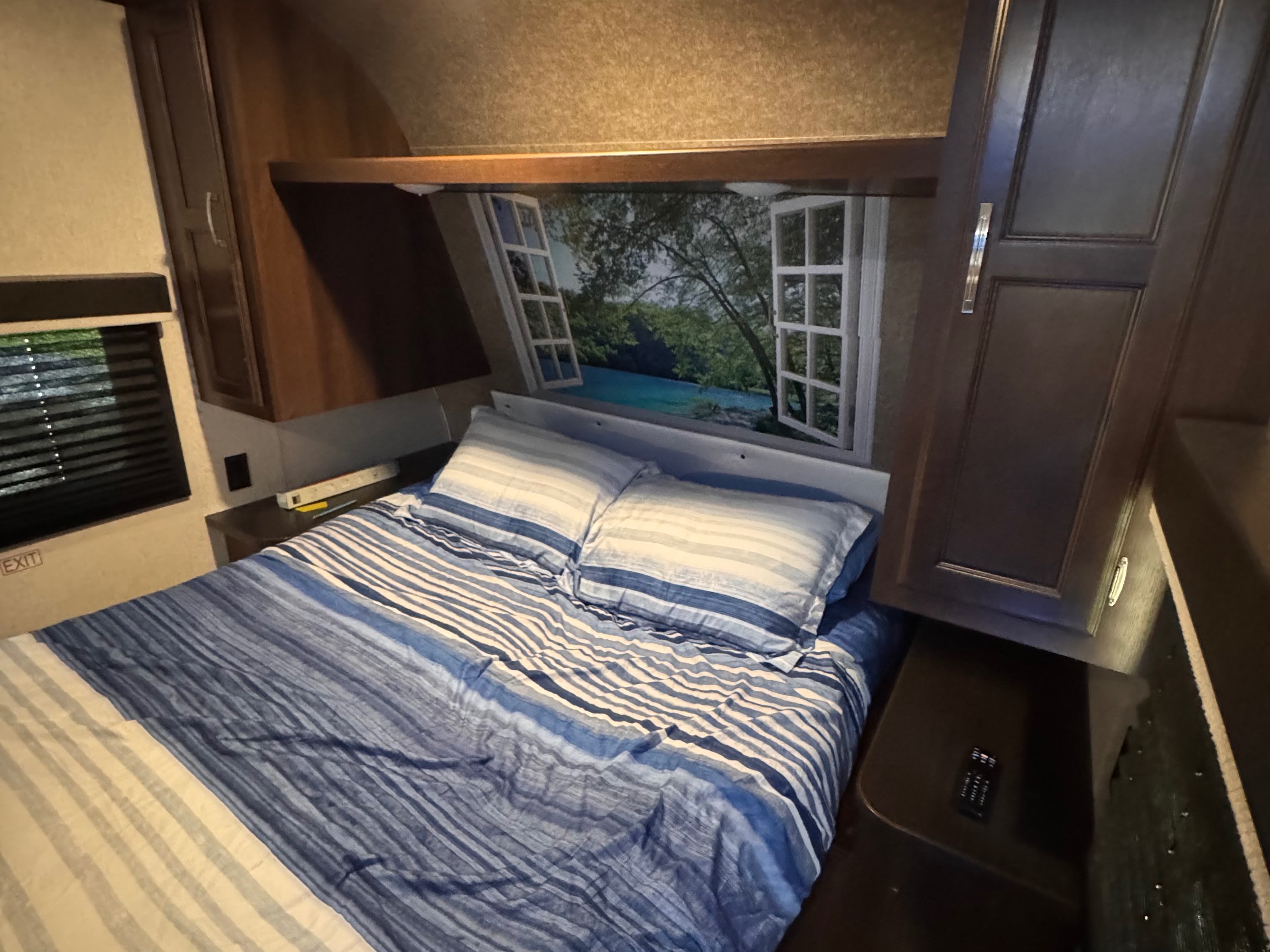 Cozy RV rental bedroom featuring blue striped bedding, a scenic window mural above the bed, and dark wood cabinets.. Jayco Jay Flight SLX 2020