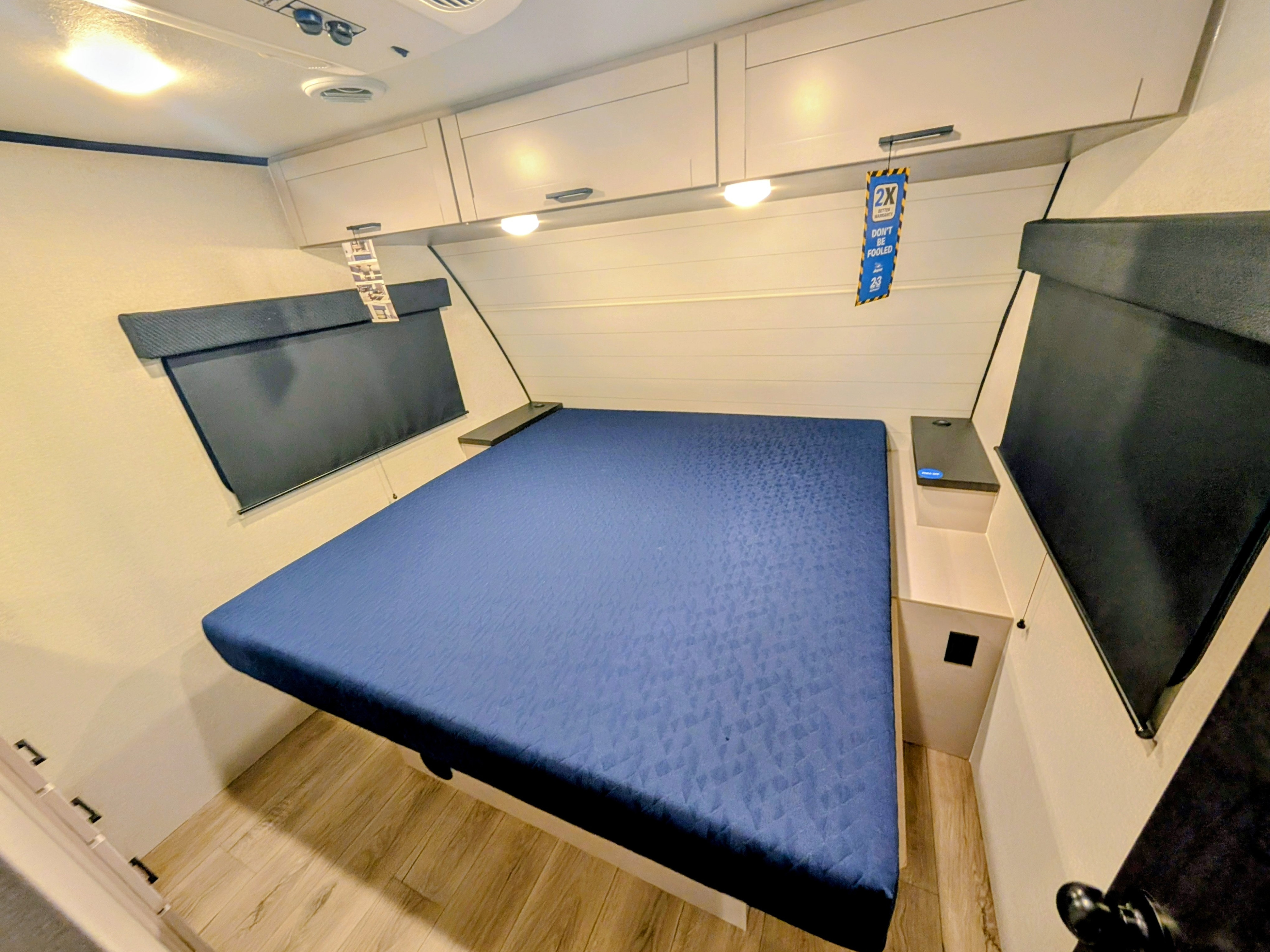 Comfortable RV rental bedroom featuring a blue bed, overhead cabinets, and window blinds for a cozy sleeping area.. Jayco Jay Feather 2026