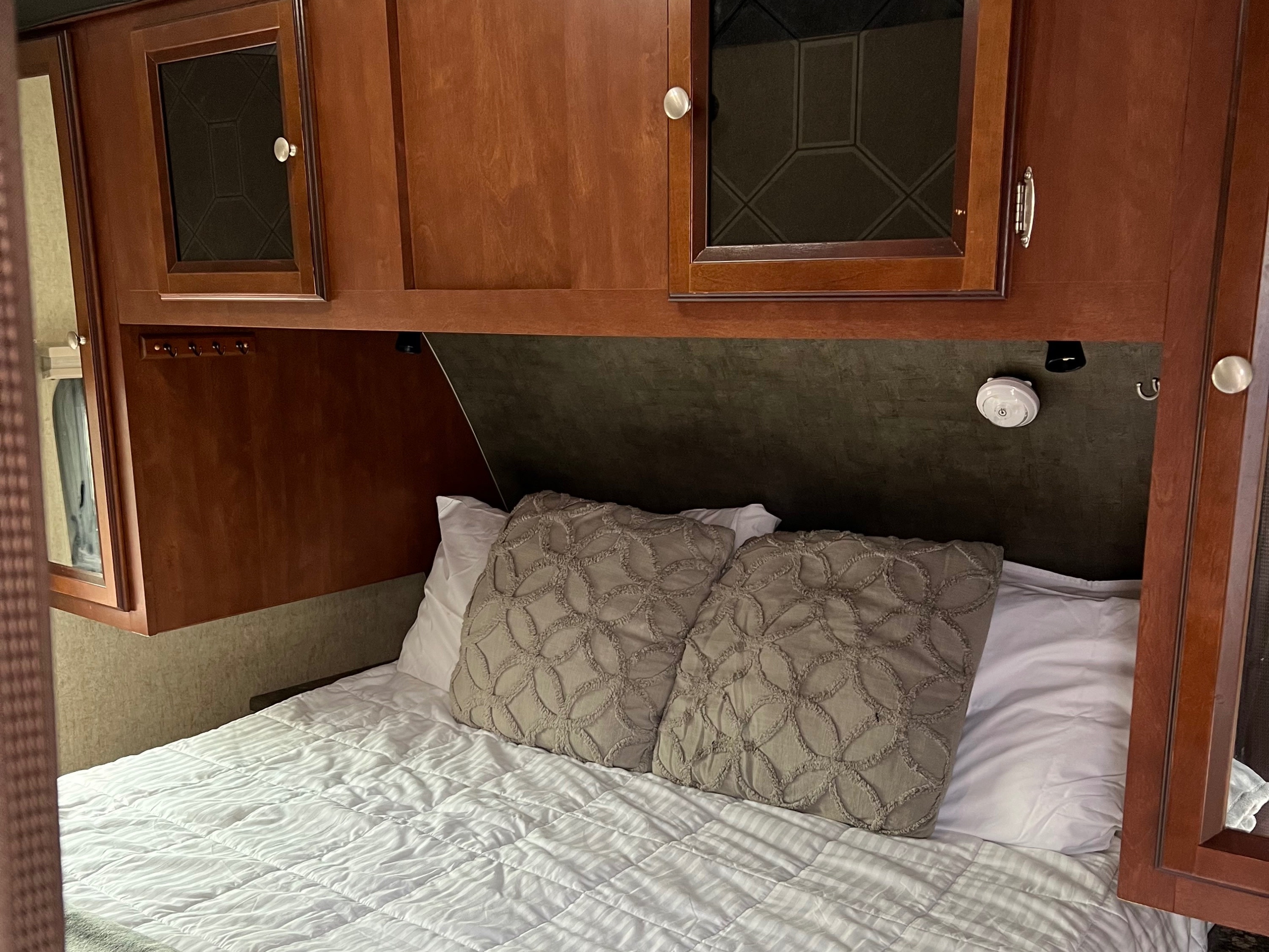 Cozy rv rental bedroom showing a bed with white bedding, grey pillows, and wooden overhead cabinets for storage.. Heartland RVs Mallard 2014