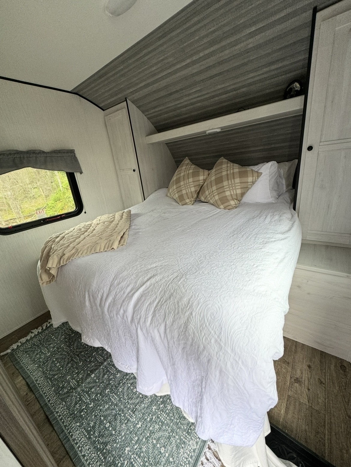 Cozy RV rental bedroom with white bedding, plaid pillows, and a window looking out to green trees, featuring a soft rug.. Forest River Cherokee 2022