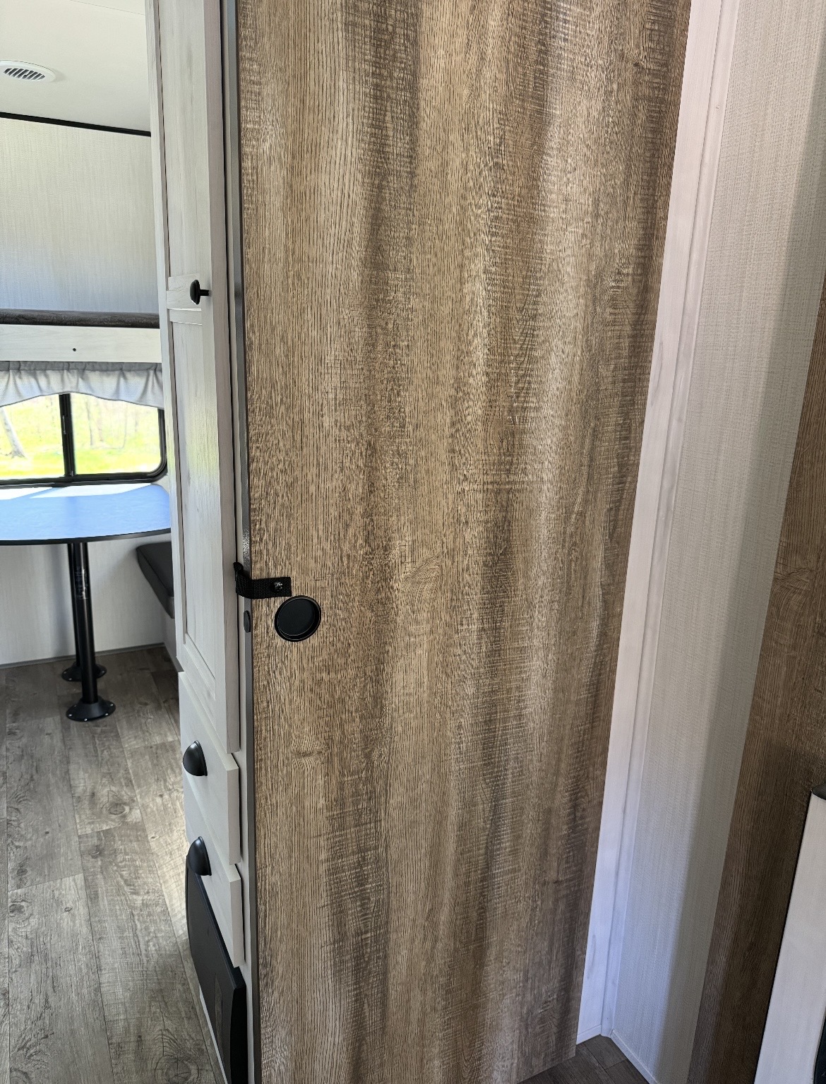 Inside an RV rental: a textured wood-look door leading to a dinette area with window and bunk beds. Light-colored interior.. Forest River Cherokee 2022