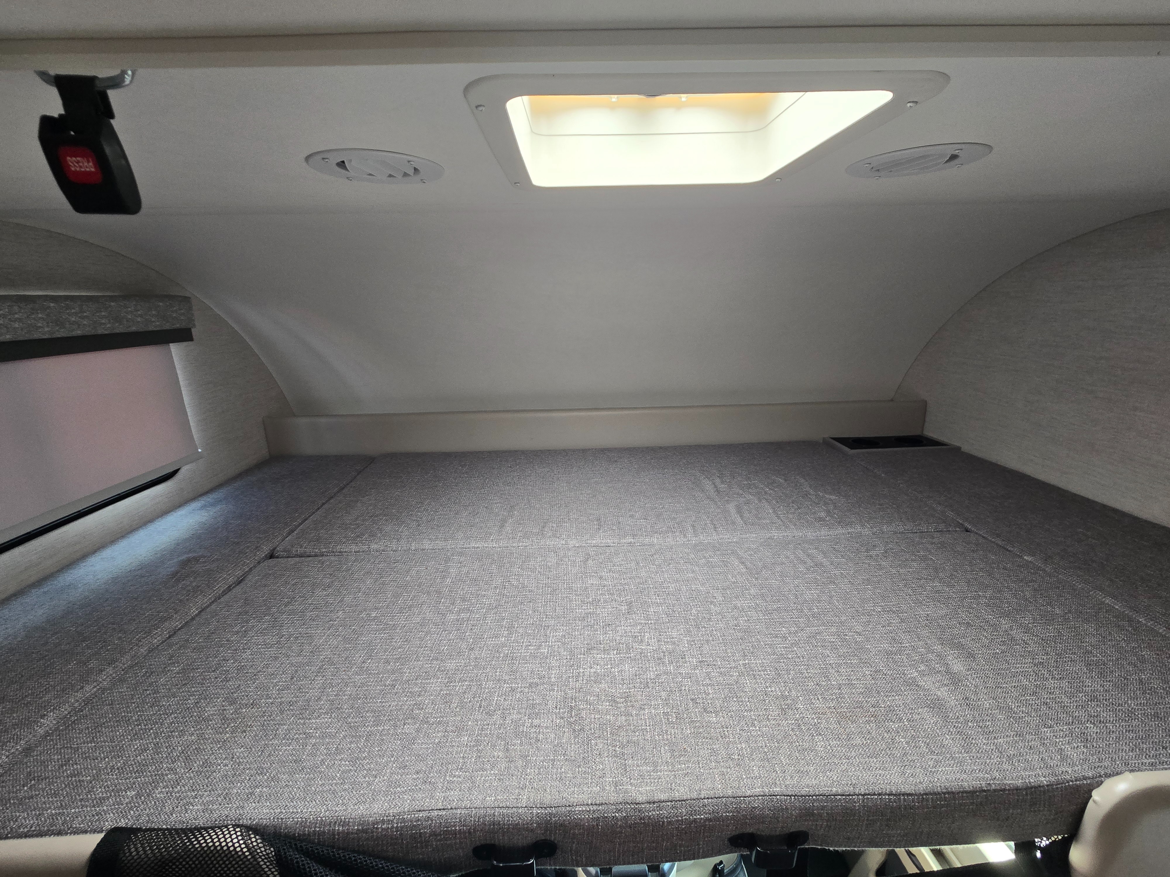 RV rental overhead bunk bed with safety buckle, skylight, window shade, cup holders, and ceiling vents.. Thor Four Winds 2025