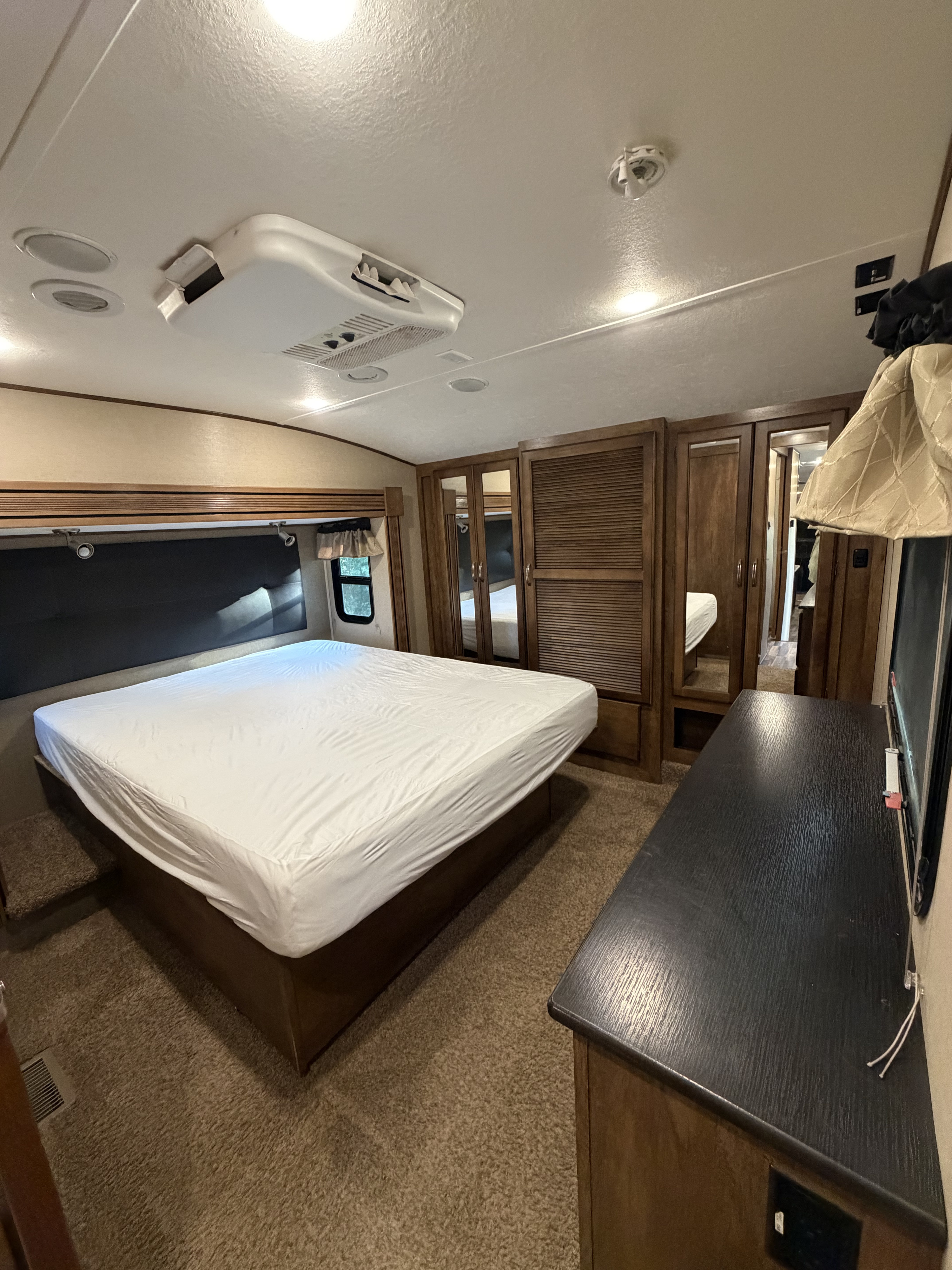Bedroom in an RV rental, showing a bed with white sheets, wooden cabinets, ceiling AC, and a dresser.. Forest River Coachmen Chaparral 2015
