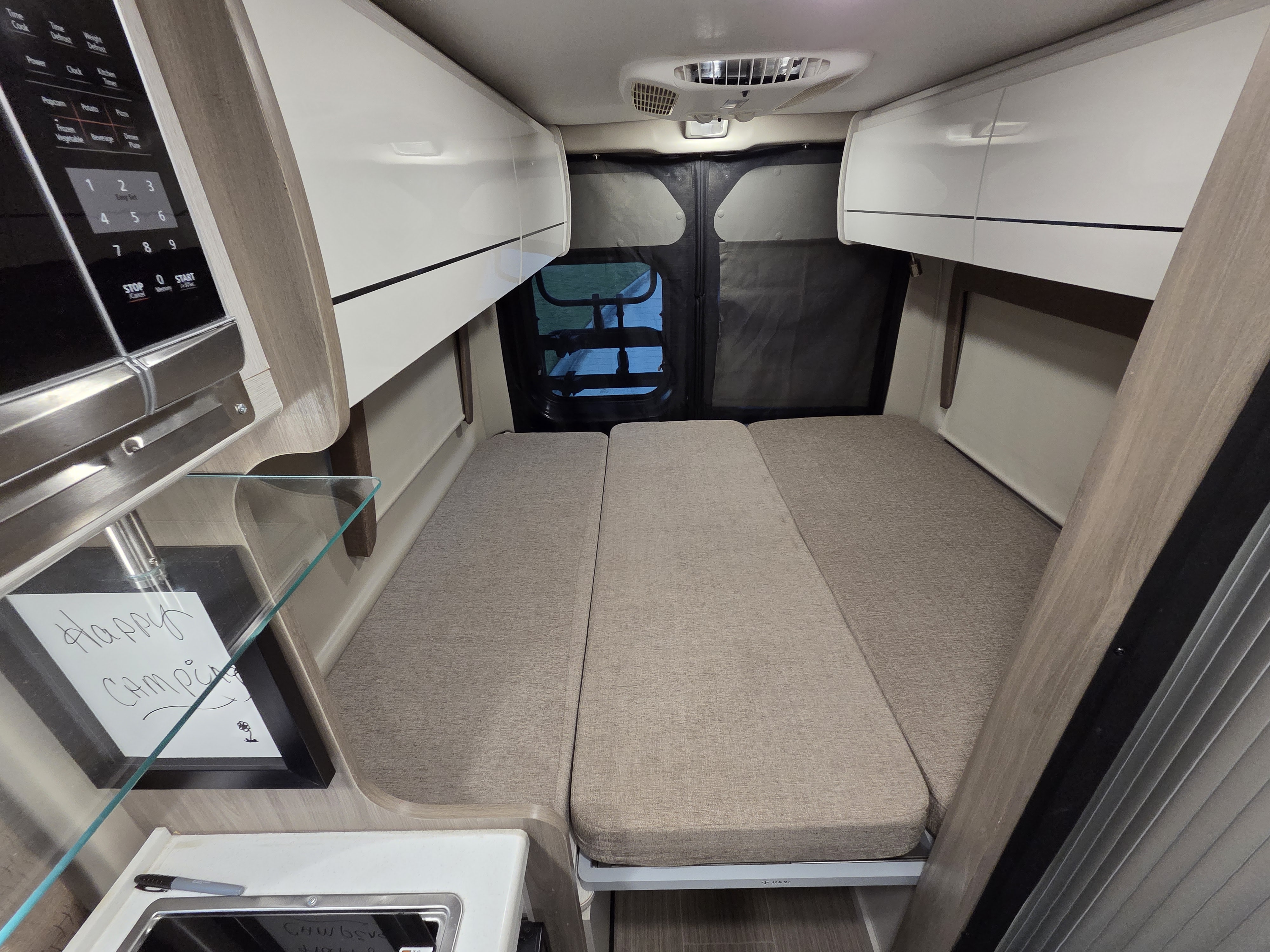 Inside a compact rv rental: a neatly made bed, kitchenette with microwave, and sleek overhead cabinets.. Thor Tellaro 2022