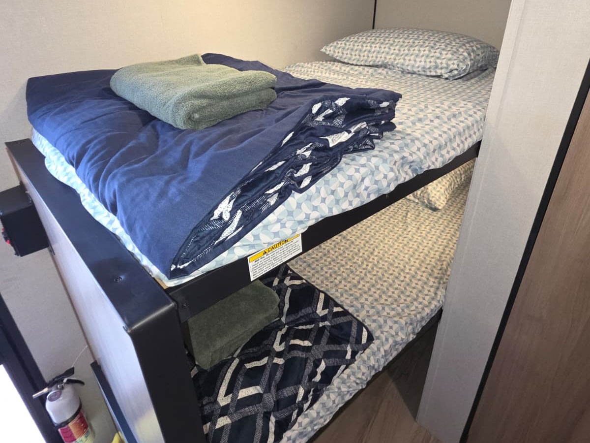 Cozy bunk beds in an RV rental, featuring blue and patterned bedding with a towel and a fire extinguisher.. Keystone RV Coleman 2026
