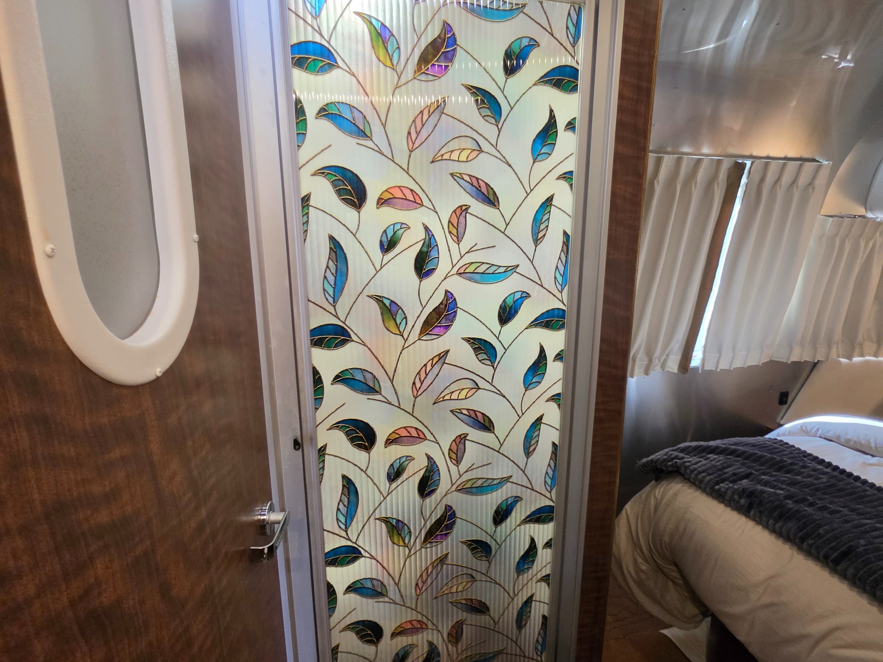 RV rental interior featuring a vibrant leaf-patterned privacy door next to a cozy bedroom with shiny aluminum details.. Airstream Globetrotter 2021