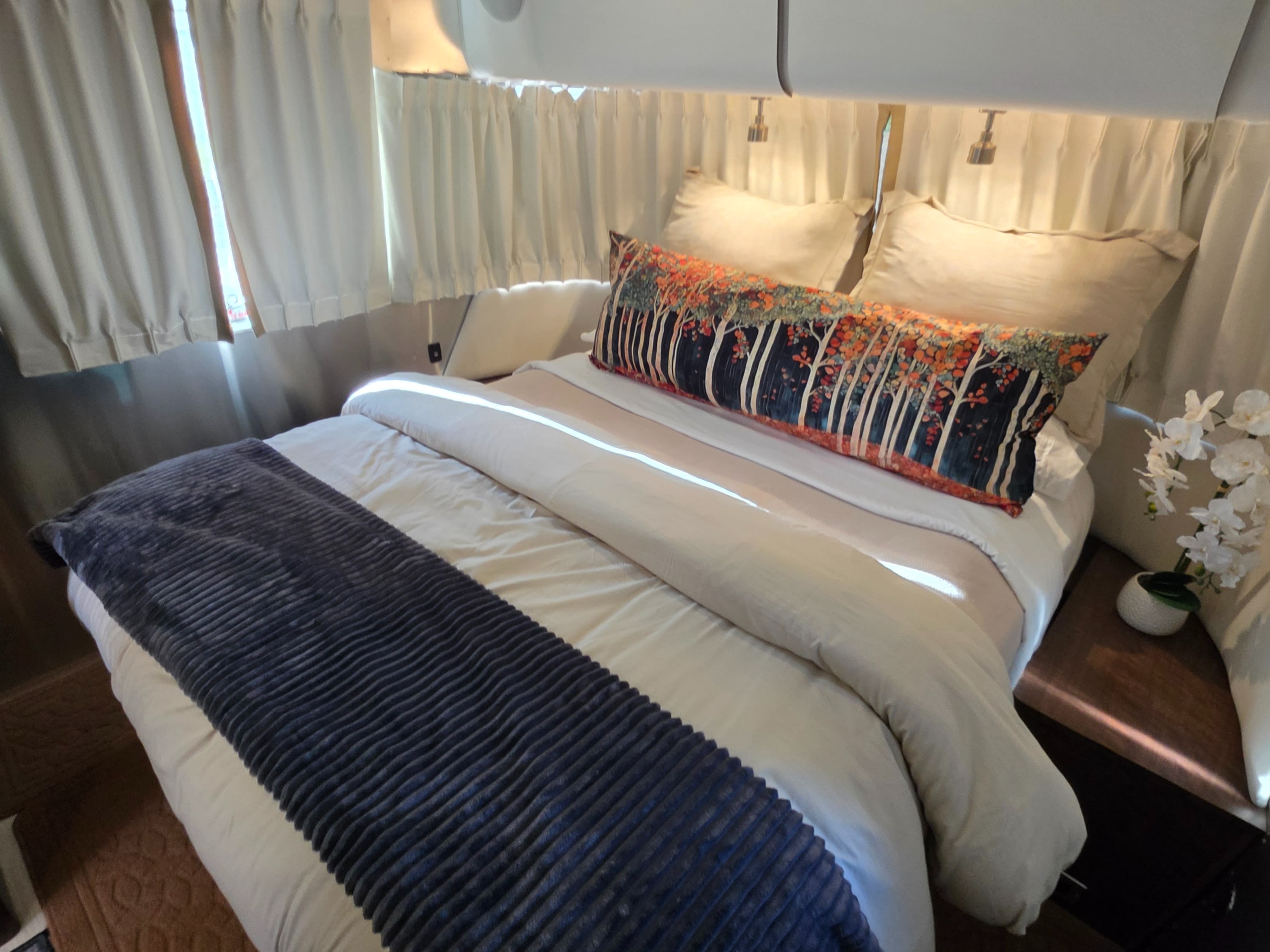 Comfortable RV rental bed with cozy bedding, a forest pillow, and reading lights, perfect for a relaxing trip.. Airstream Globetrotter 2021
