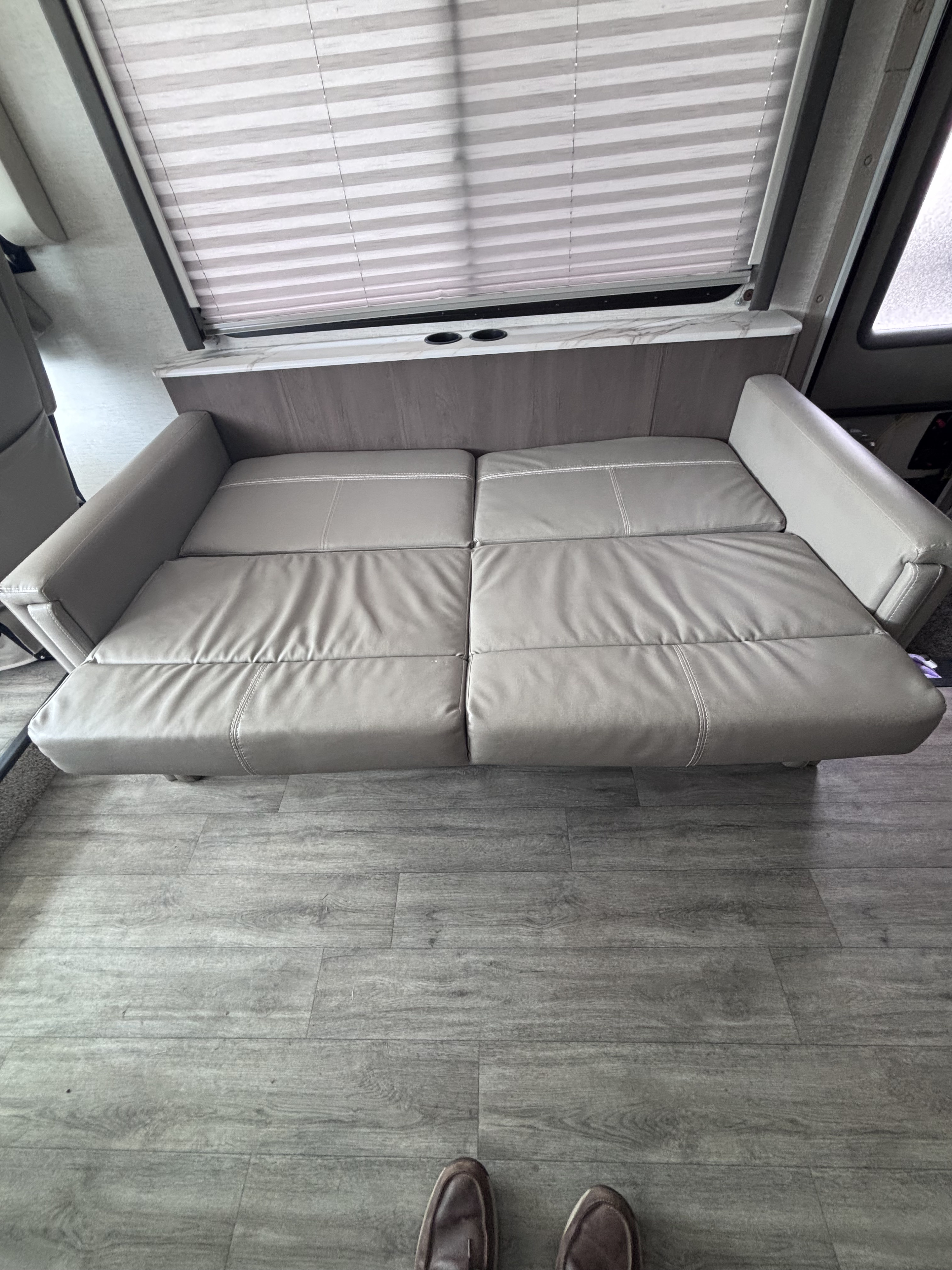 Relax in this rv rental! View of a comfortable gray sofa bed extended, with window blinds, cup holders, and laminate flooring.. Thor Resonate 2024