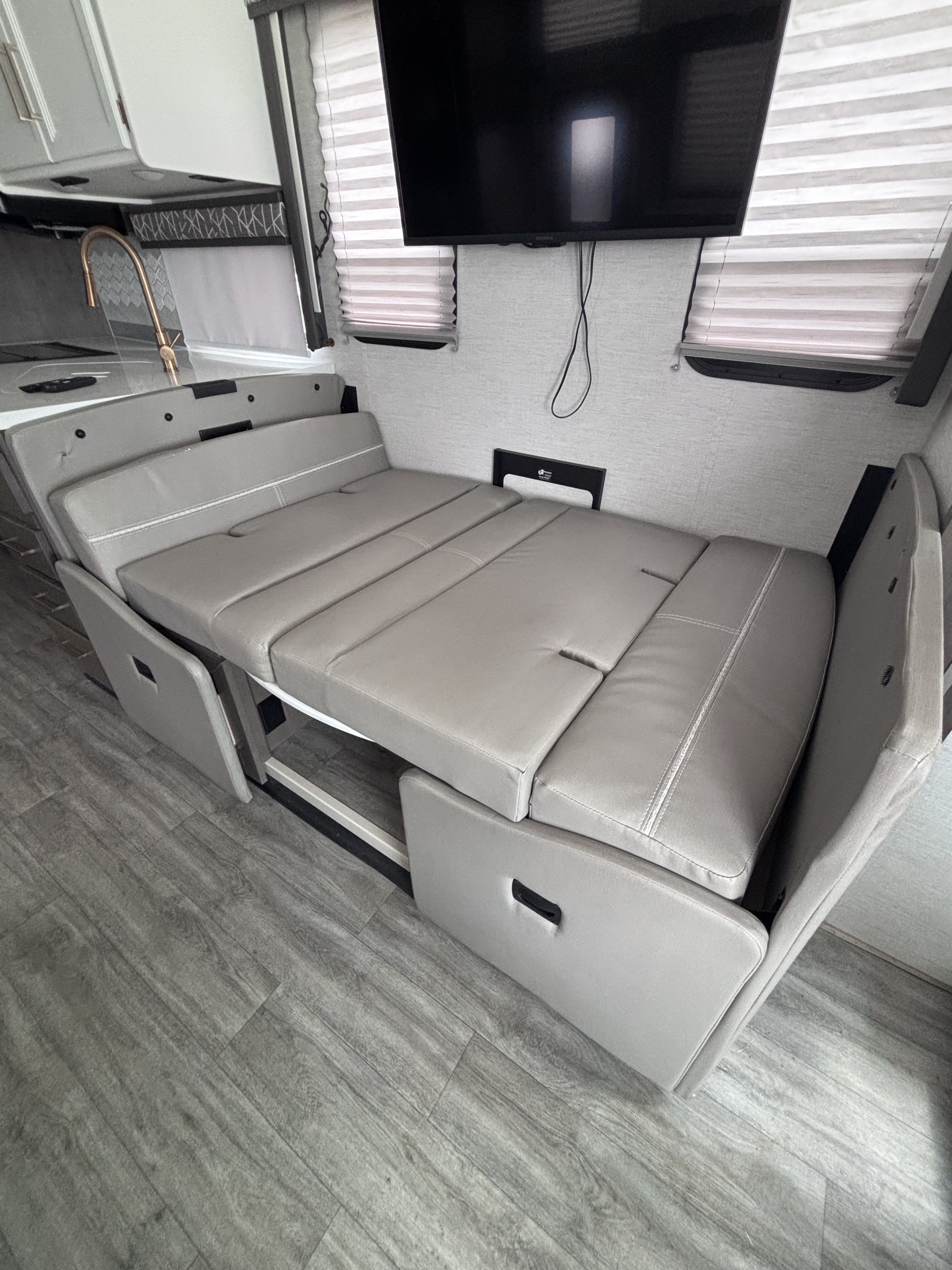 RV rental: light grey convertible dinette as a bed, with kitchen, TV, and modern wood-look flooring in a cozy interior.. Thor Resonate 2024
