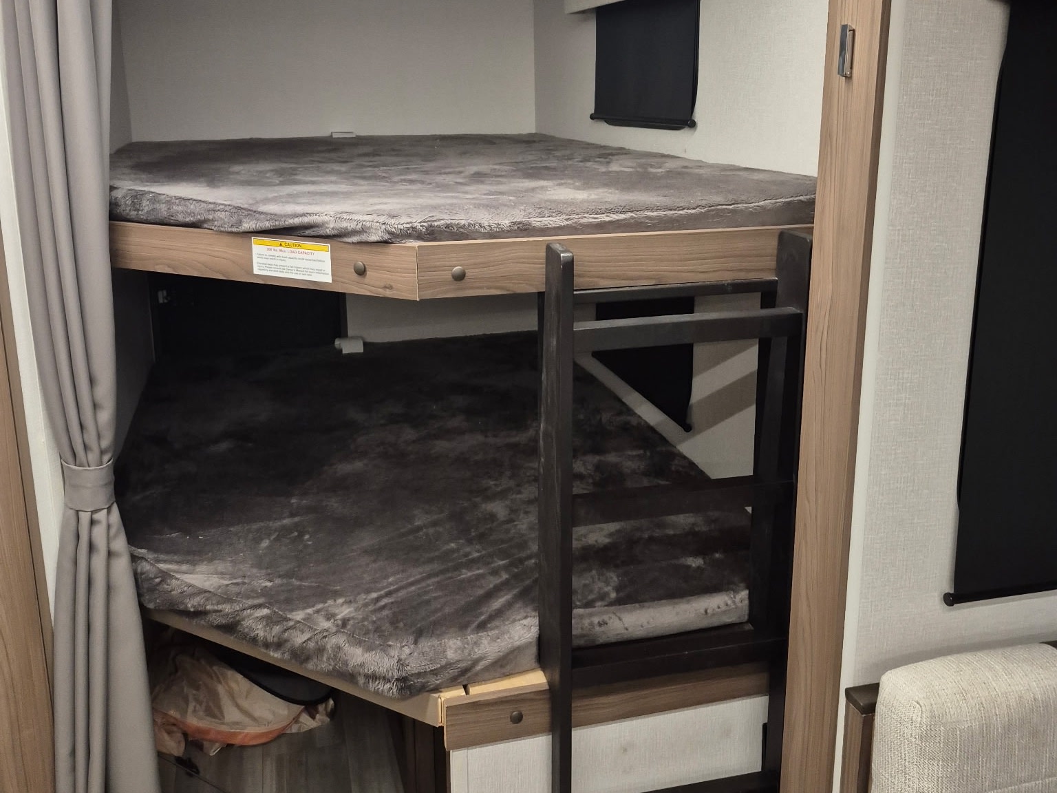 Cozy bunk beds in an RV rental, featuring soft grey blankets, a safety ladder, and privacy curtains.. Wayfinder Go Explore X252 2025