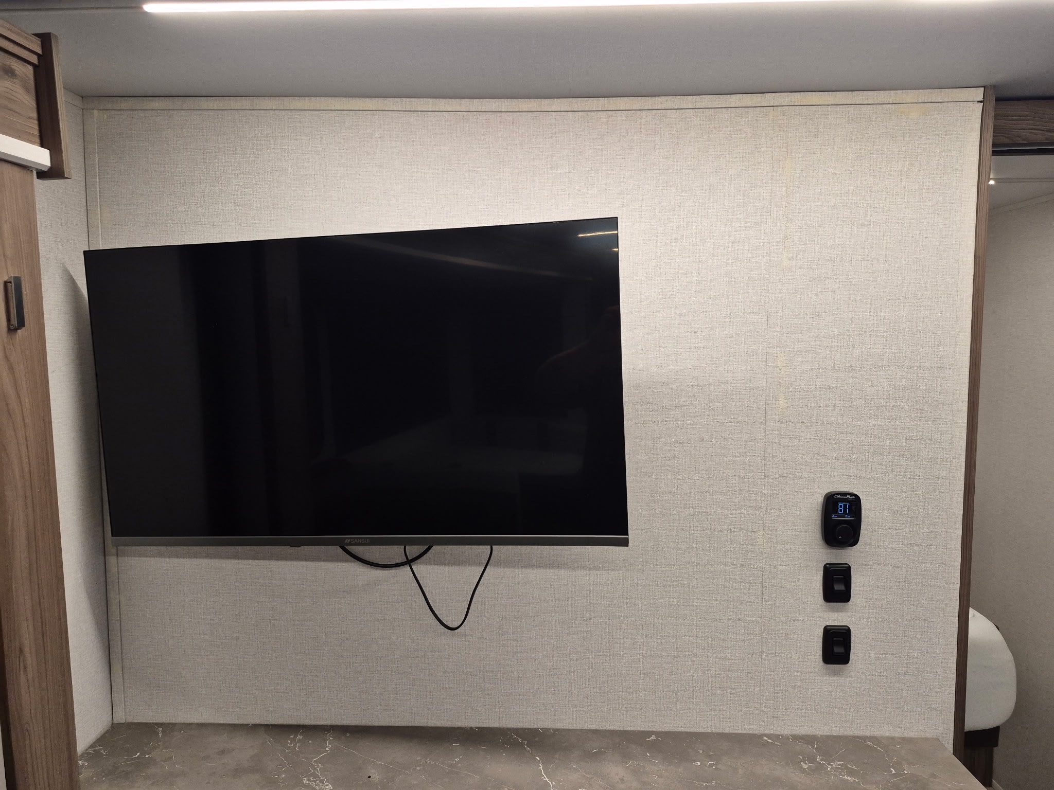 Modern RV rental interior with a wall-mounted TV, digital thermostat (81°F), and light switches above a counter.. Wayfinder Go Explore X252 2025