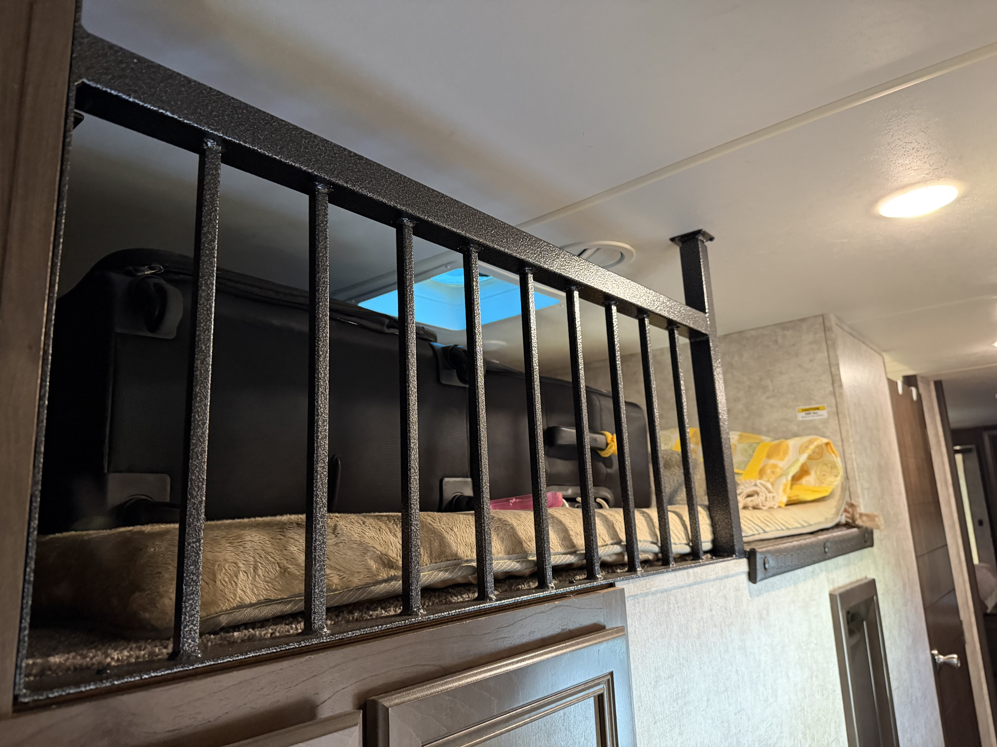 View of an RV rental bunk bed with a textured metal safety railing, soft cushion, and overhead lighting.. Highland Ridge RV Open Range 2018