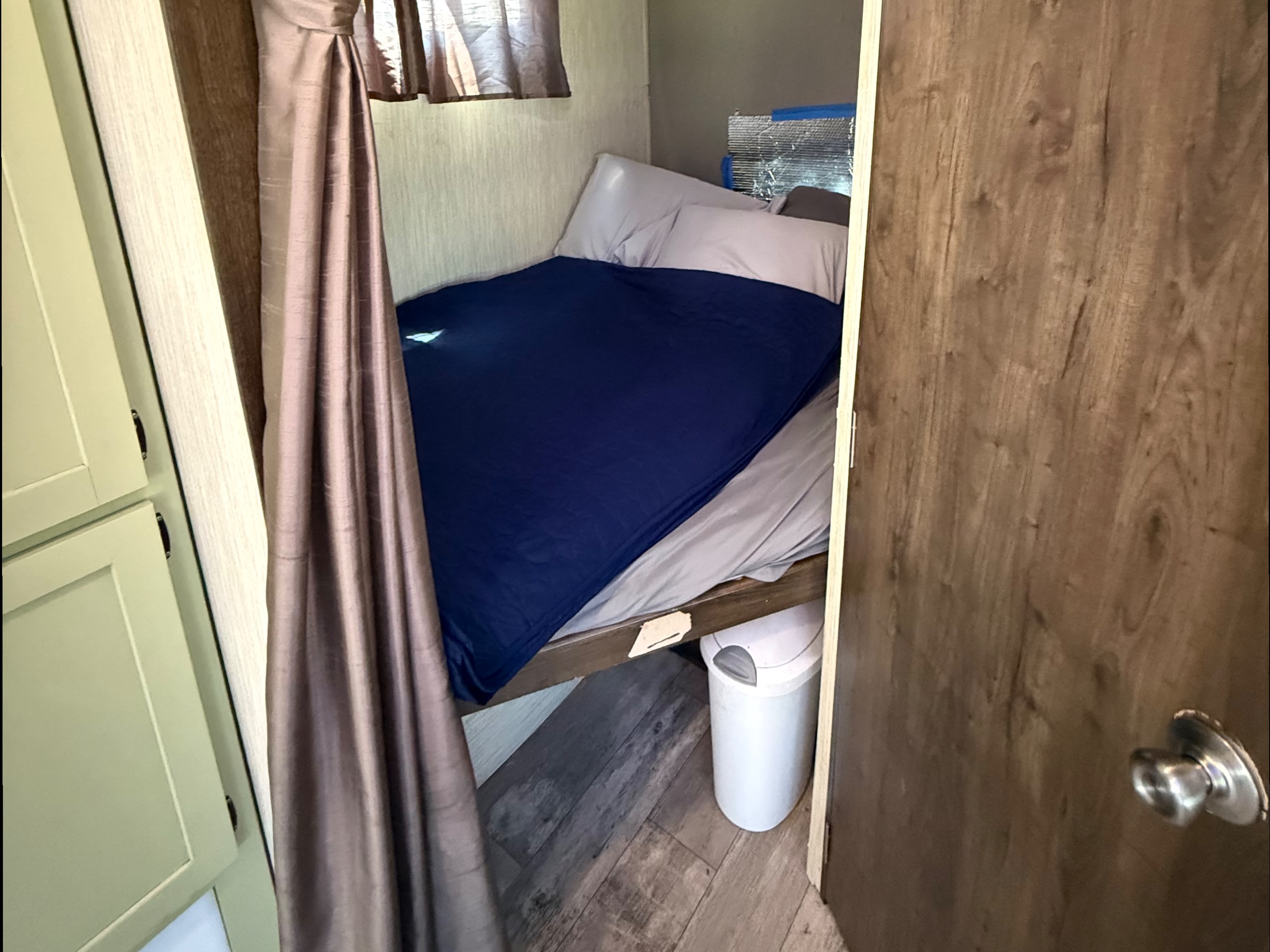 Bunk bed with blue blanket, light pillows, and insulation in a compact rv rental space. A small trash can is below, with curtains to the side.. Crossroads RV Volante 2019