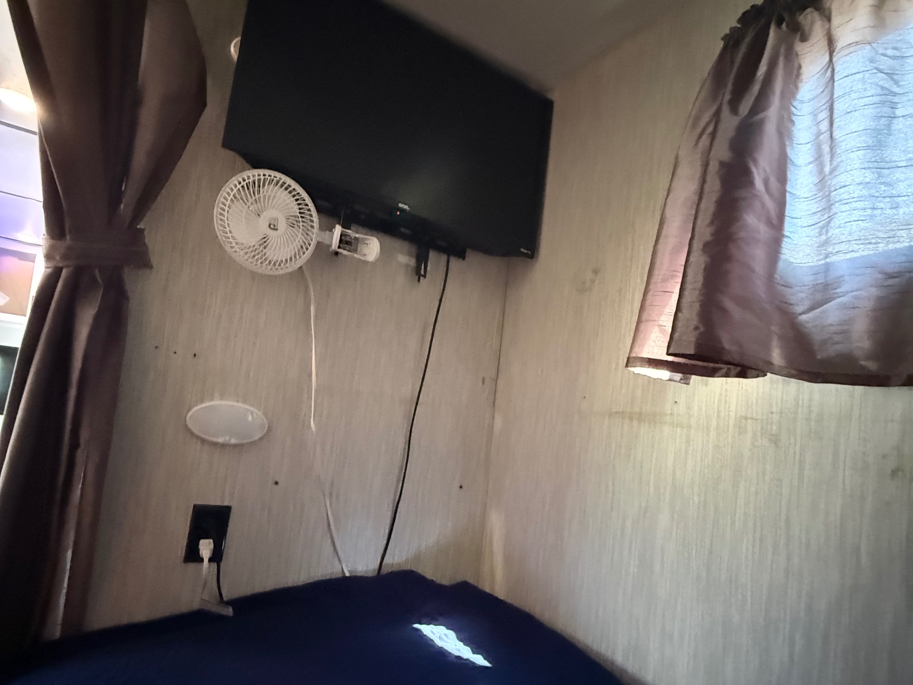 An rv rental interior featuring a wall-mounted TV, small fan, and draped curtains, with a power outlet and bed visible.. Crossroads RV Volante 2019