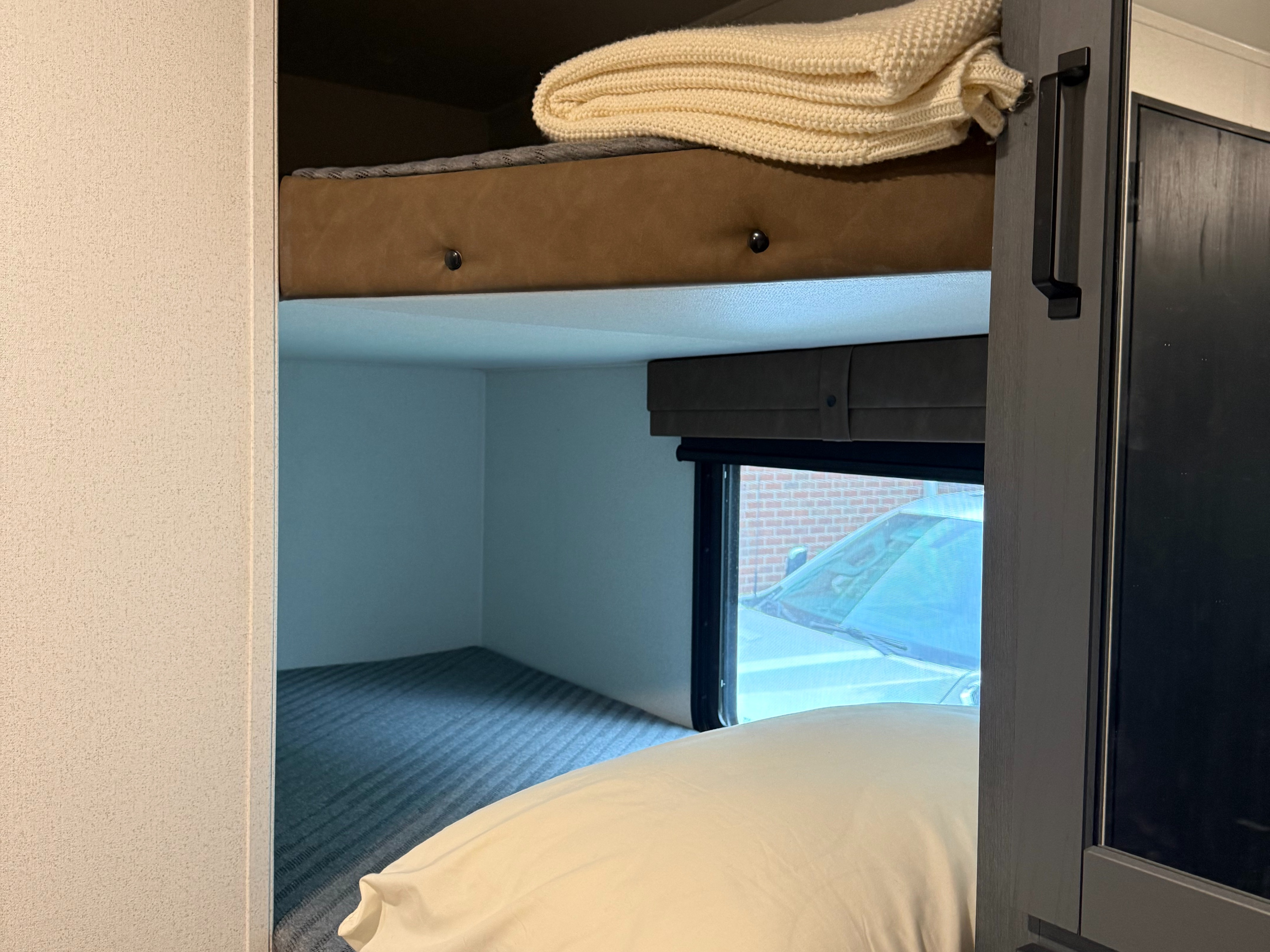 Relax in this RV rental's cozy bunk beds. Features a top bunk with a blanket, a bottom bunk with a pillow, and a window.. Forest River Palomino Puma 2026