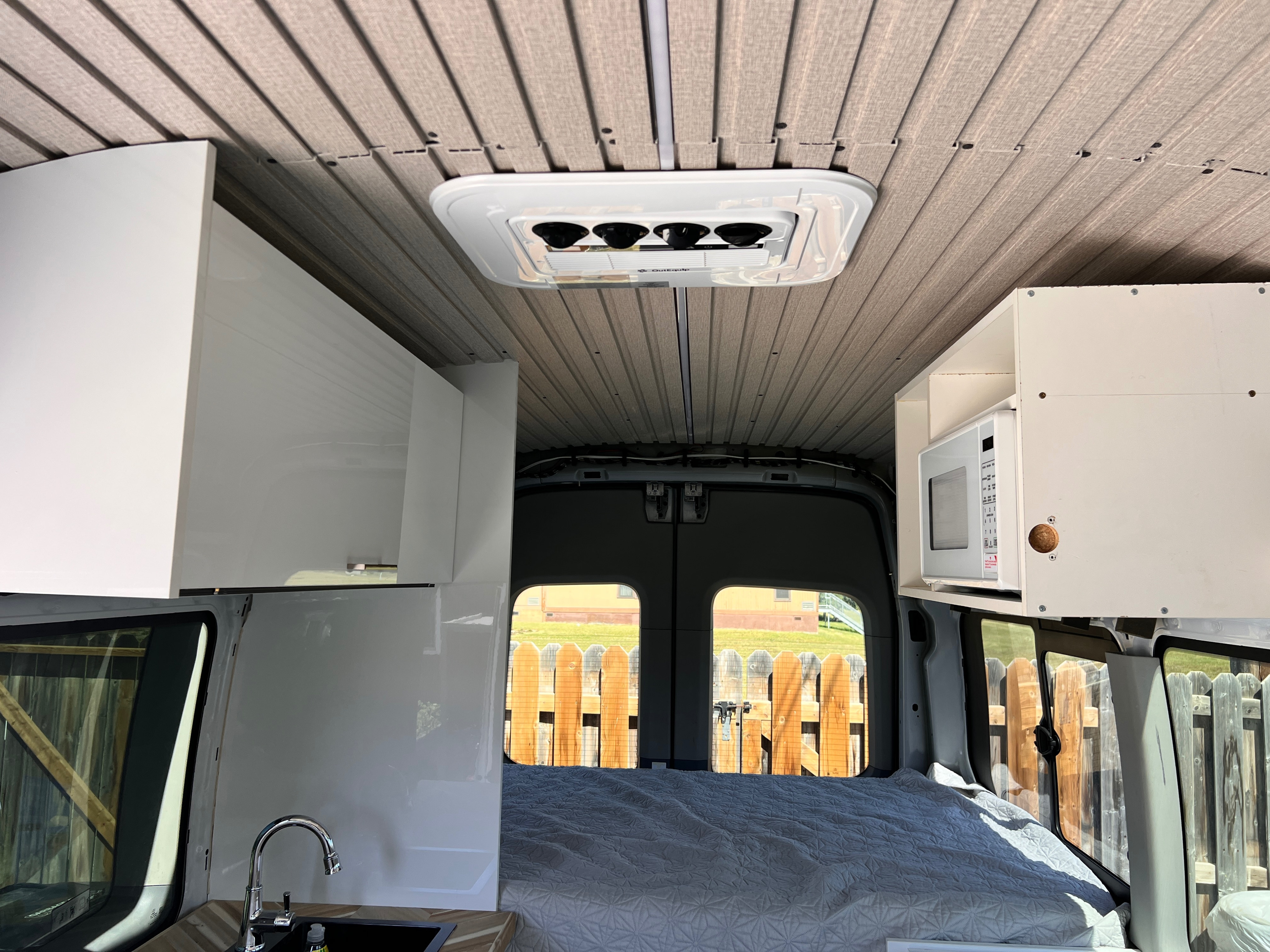 RV rental interior with overhead AC, microwave, sink, and bed, showing a cozy van conversion.. Ford Transit 2016