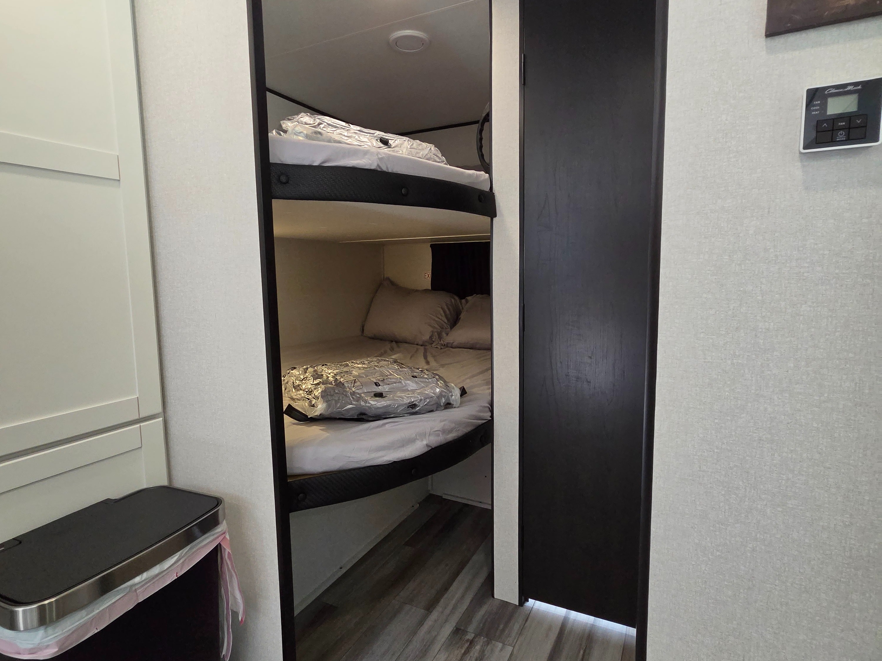 This RV rental features a bunk bed area with two beds, each with new, plastic-wrapped bedding. A thermostat and small trash bin are also visible.. Jayco Jay Flight SLX 2026